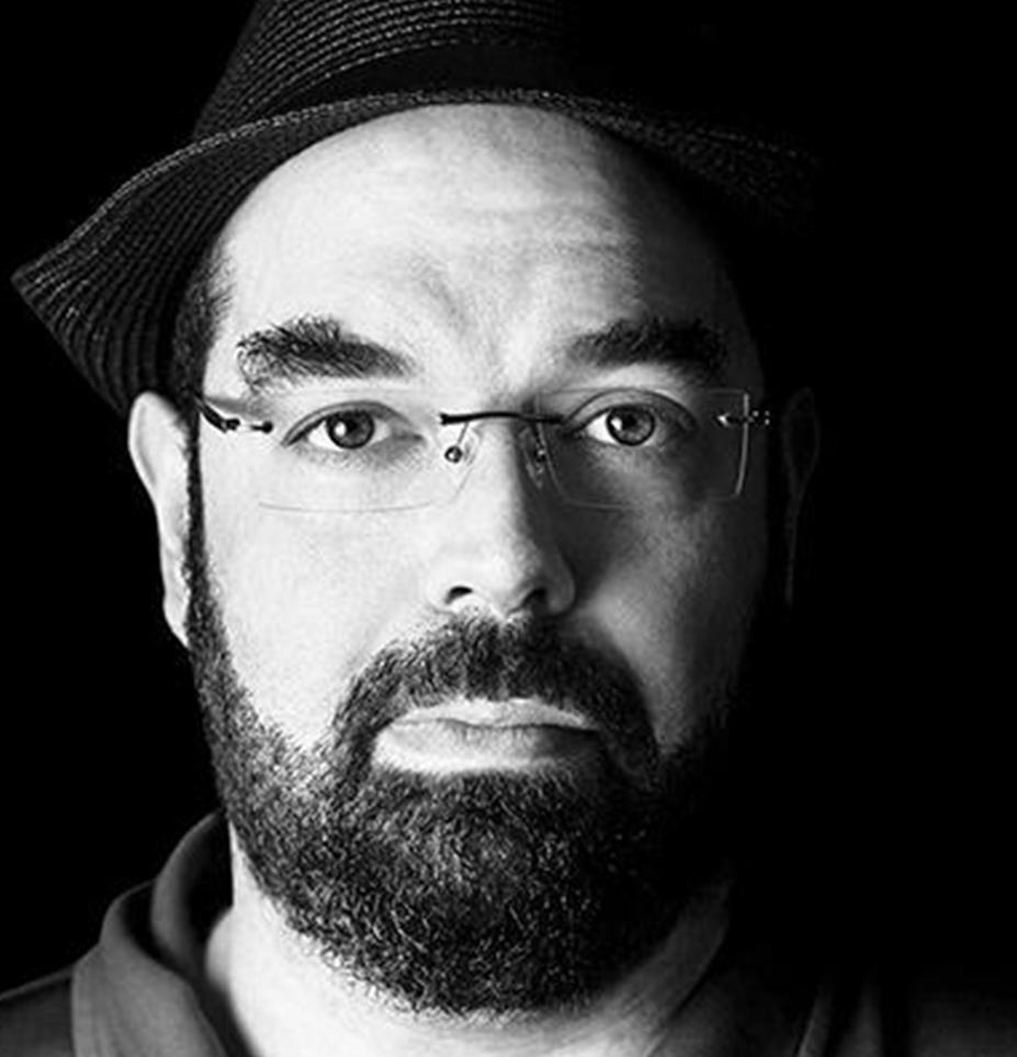 Black and white portrait photo of Eliezer Yudkowsky with glasses, a beard, and a mustache, wearing a fedora hat.