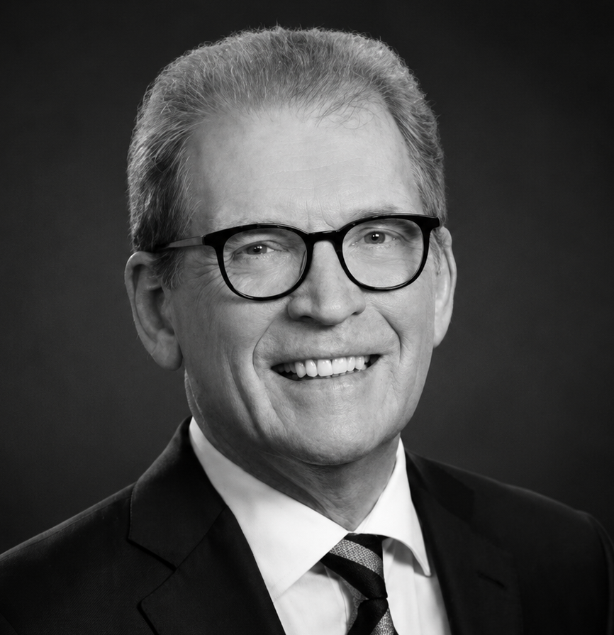 Black and white portrait of a smiling Lloyd Minor with glasses, wearing a suit and tie.