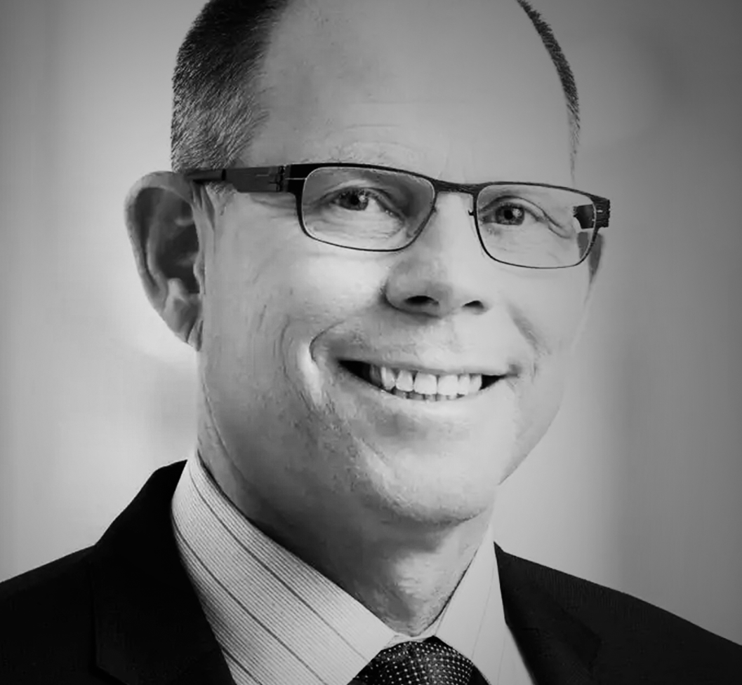 Black and white professional headshot of a smiling Mark Suzman wearing glasses, a suit, and a tie.