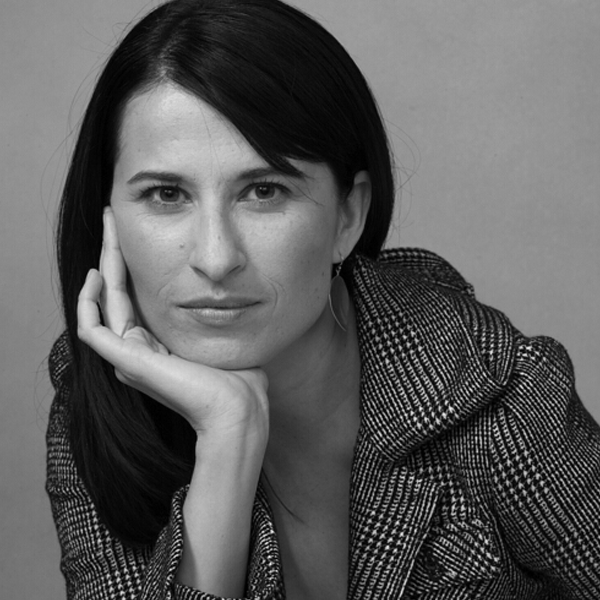 Black and white portrait of Sheelah Kolhatkar with dark hair wearing a patterned jacket, resting her chin on her hand, looking directly at the camera.