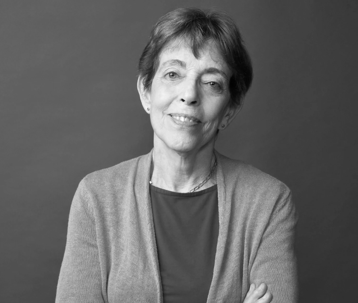 Black and white portrait of a smiling Shanna Swan, wearing a cardigan and a necklace, against a plain background.