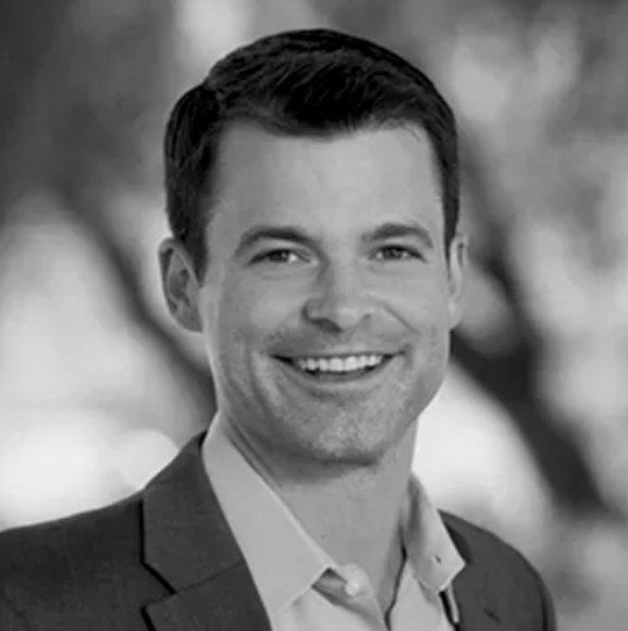 A smiling Robb Willer in a suit in a close-up portrait, black and white.