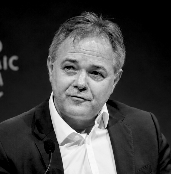 Black and white photo of Sir Jeremy Farrar with light-colored hair, wearing a suit and white shirt, sitting and making a face during a discussion.