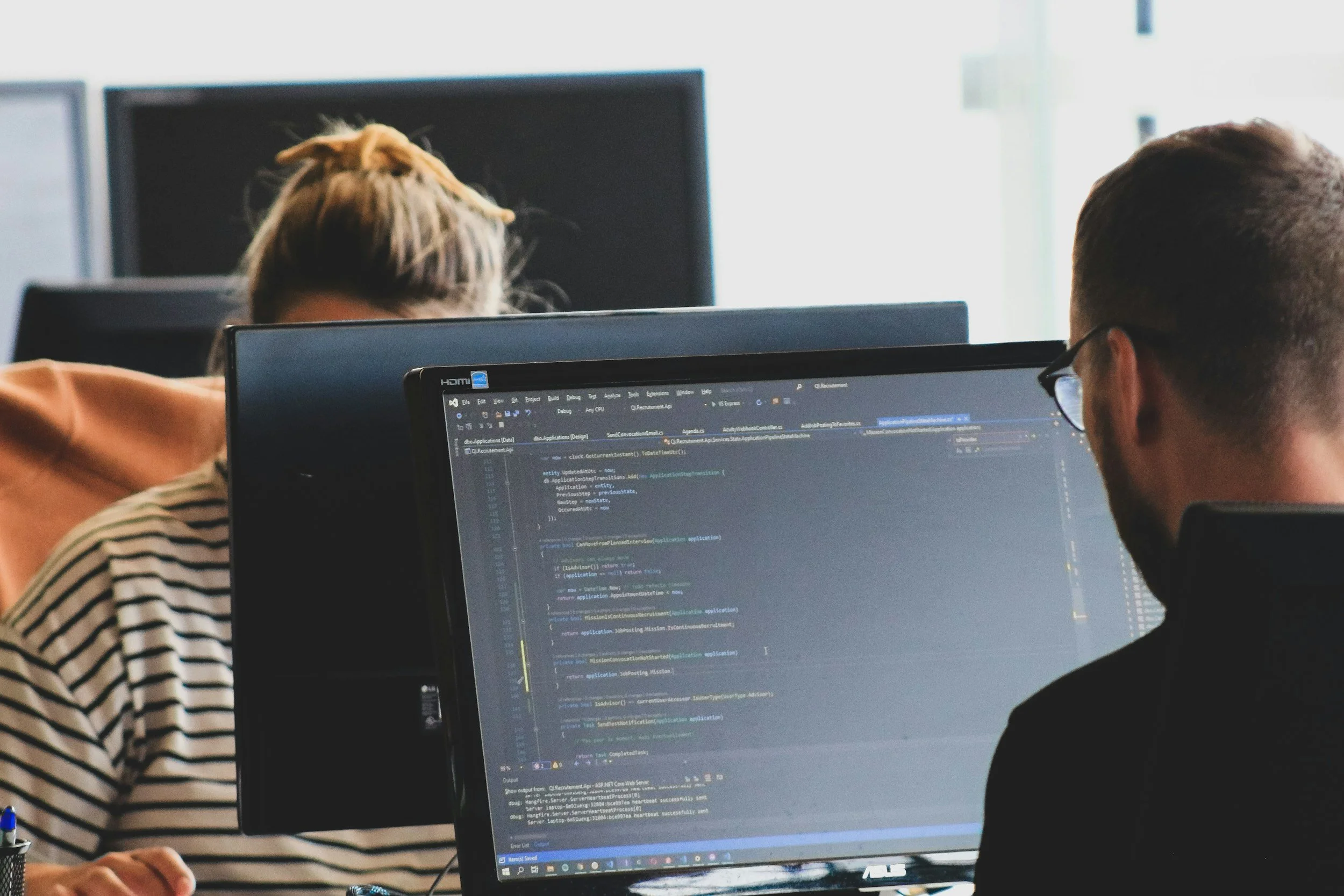 People working on computers in an office, with code visible on the screens. An image that represents managed IT Support.