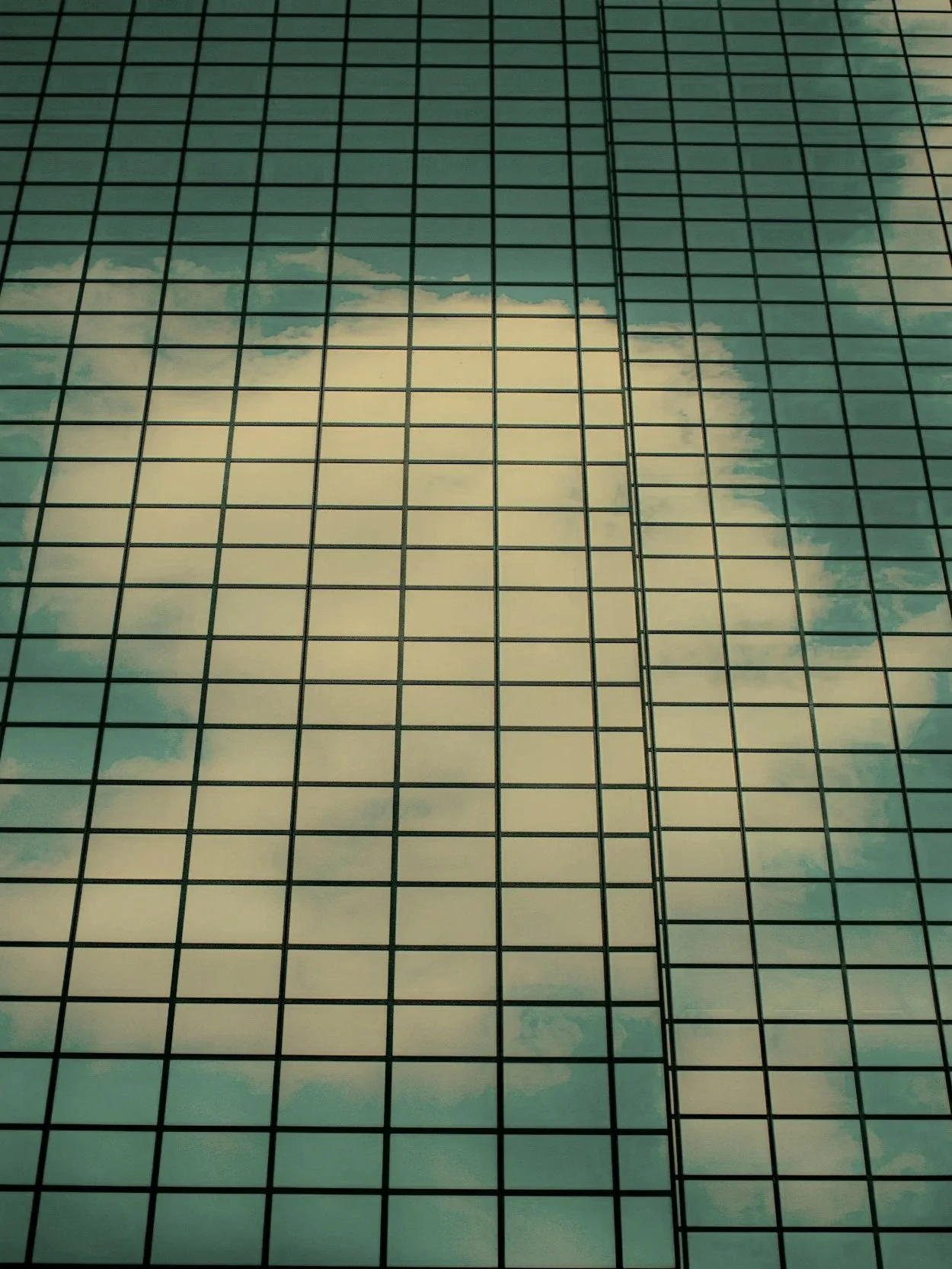 Reflection of a cloudy sky on the glass facade of a tall office building. An image representing structured cloud technology.