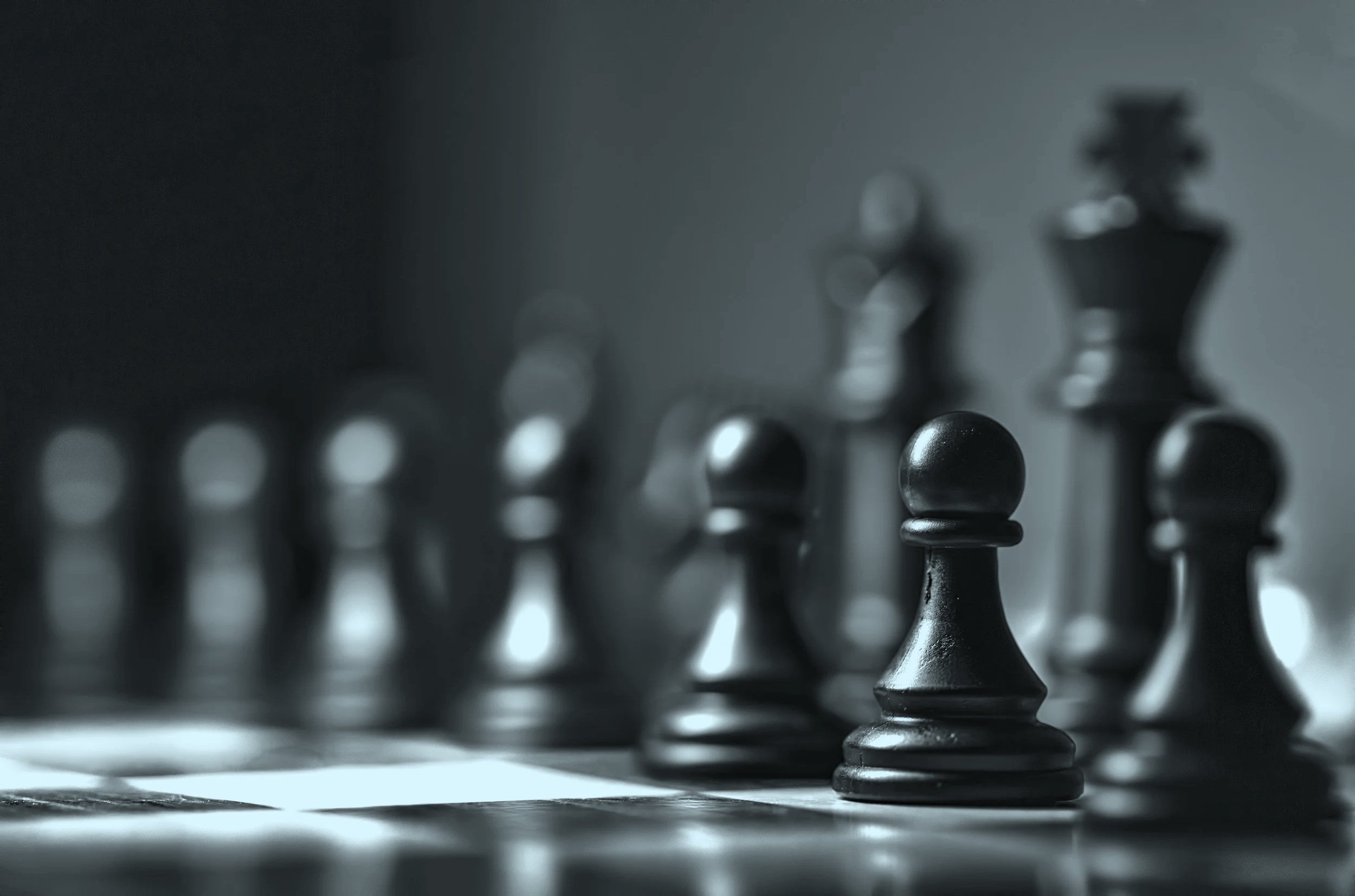 Close-up of a chessboard with black chess pieces, including a king and queen, in focus, while the other pieces are blurred in the background. An image that represents vCISO (virtual CISO) and strategic information security services.