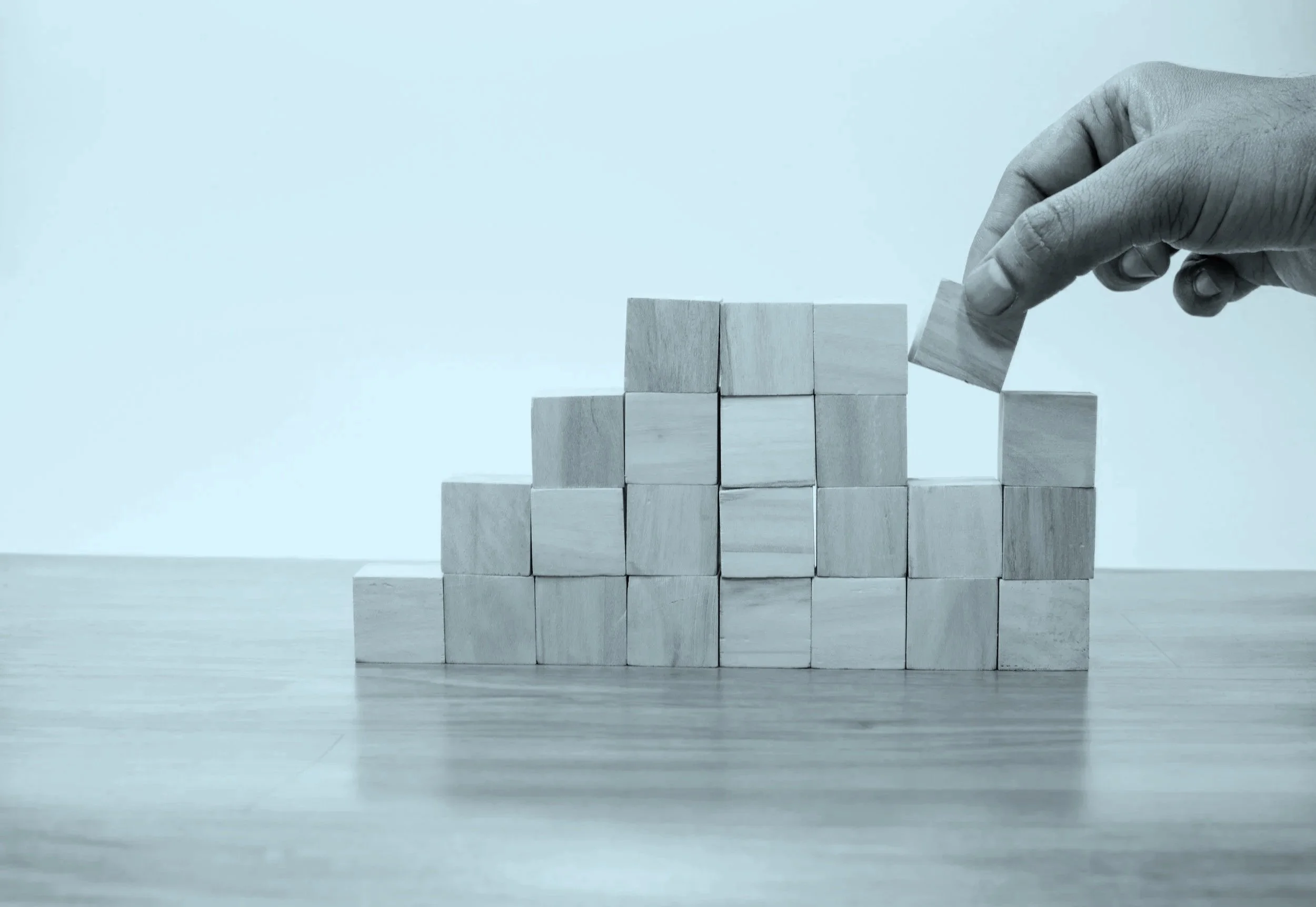 A hand stacking small wooden blocks on a flat surface against a plain background. A general image that represents cloud security posture management.