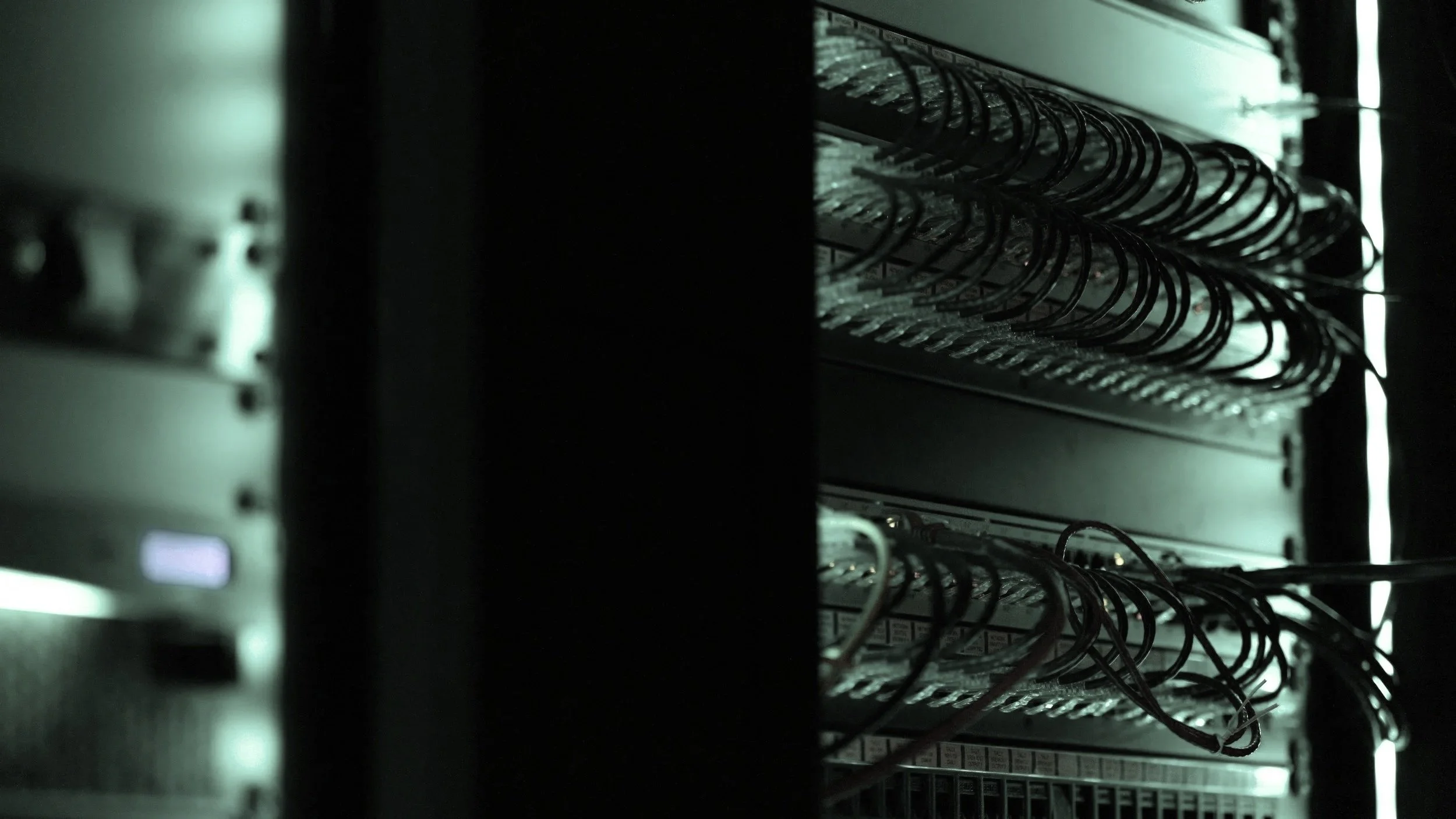 A close-up of a server rack with multiple network cables connected to it, in a dimly lit environment. A representation of I.T and Network technology.