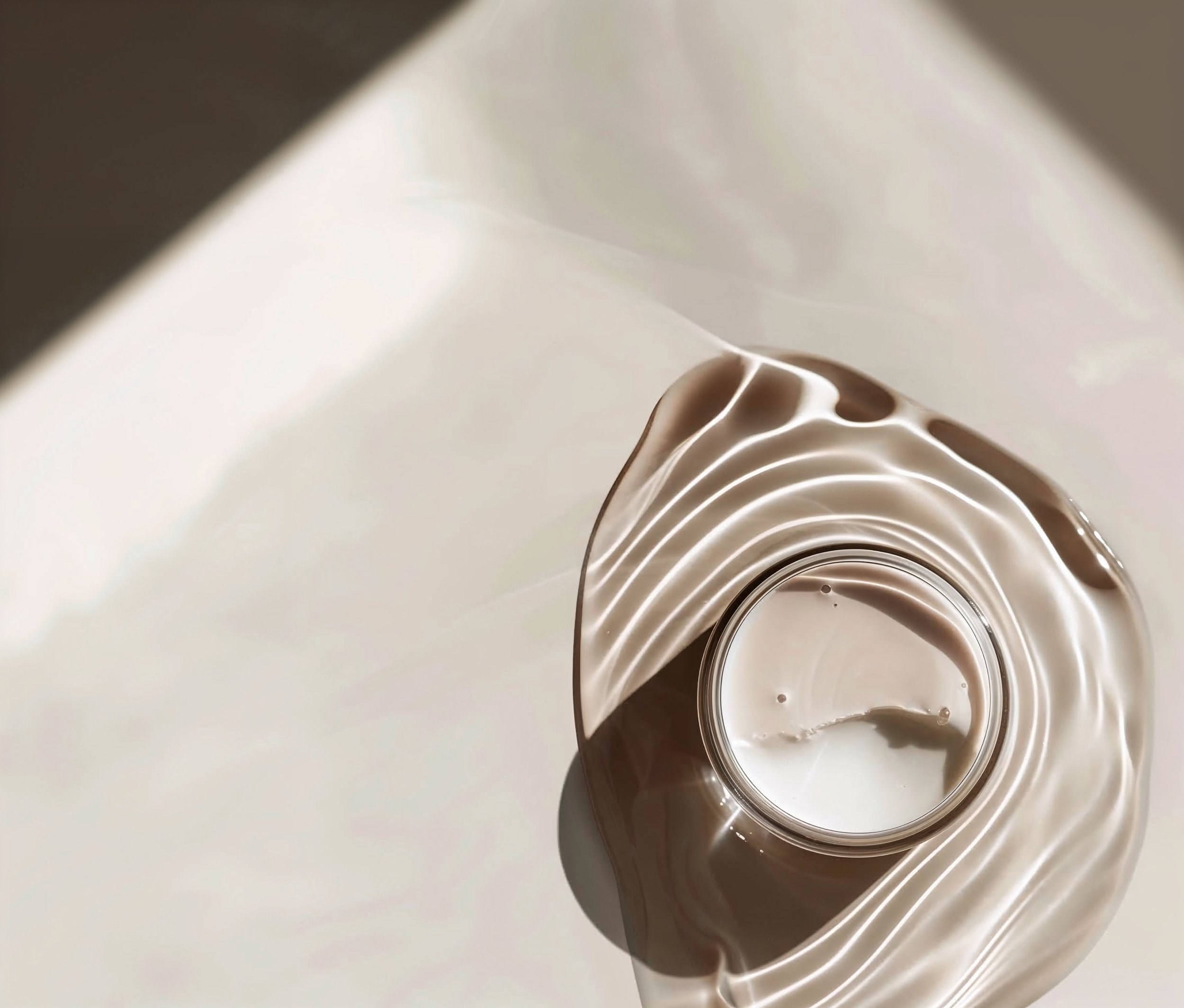 A top-down view of a metallic spiral-shaped object with concentric circles, reflecting light, set against a white surface.