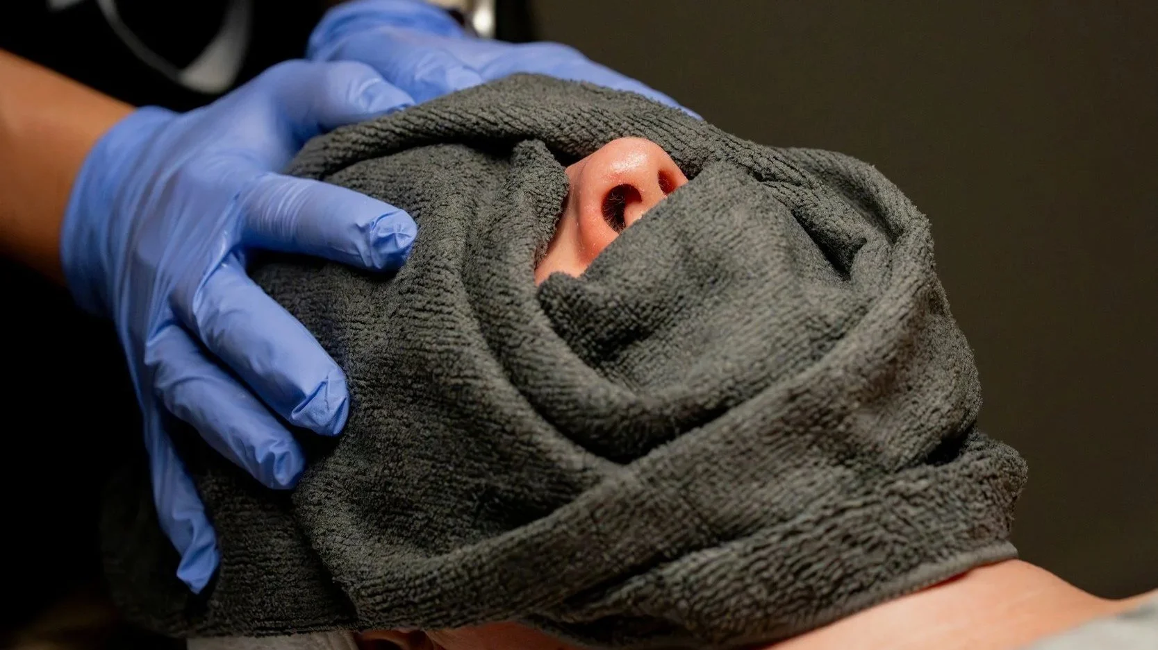 Person receiving chest compressions during CPR with a towel wrapped around their head and wearing gloves.