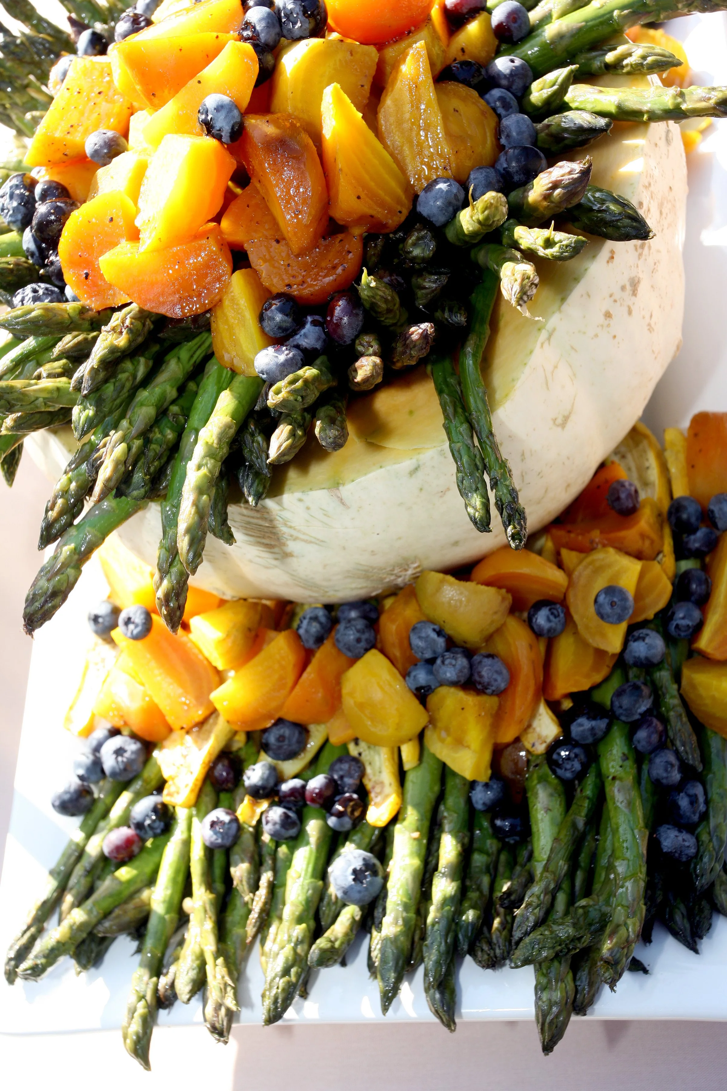 Asparagus topped with roasted butternut squash, blueberries, and chopped yellow and orange vegetables.