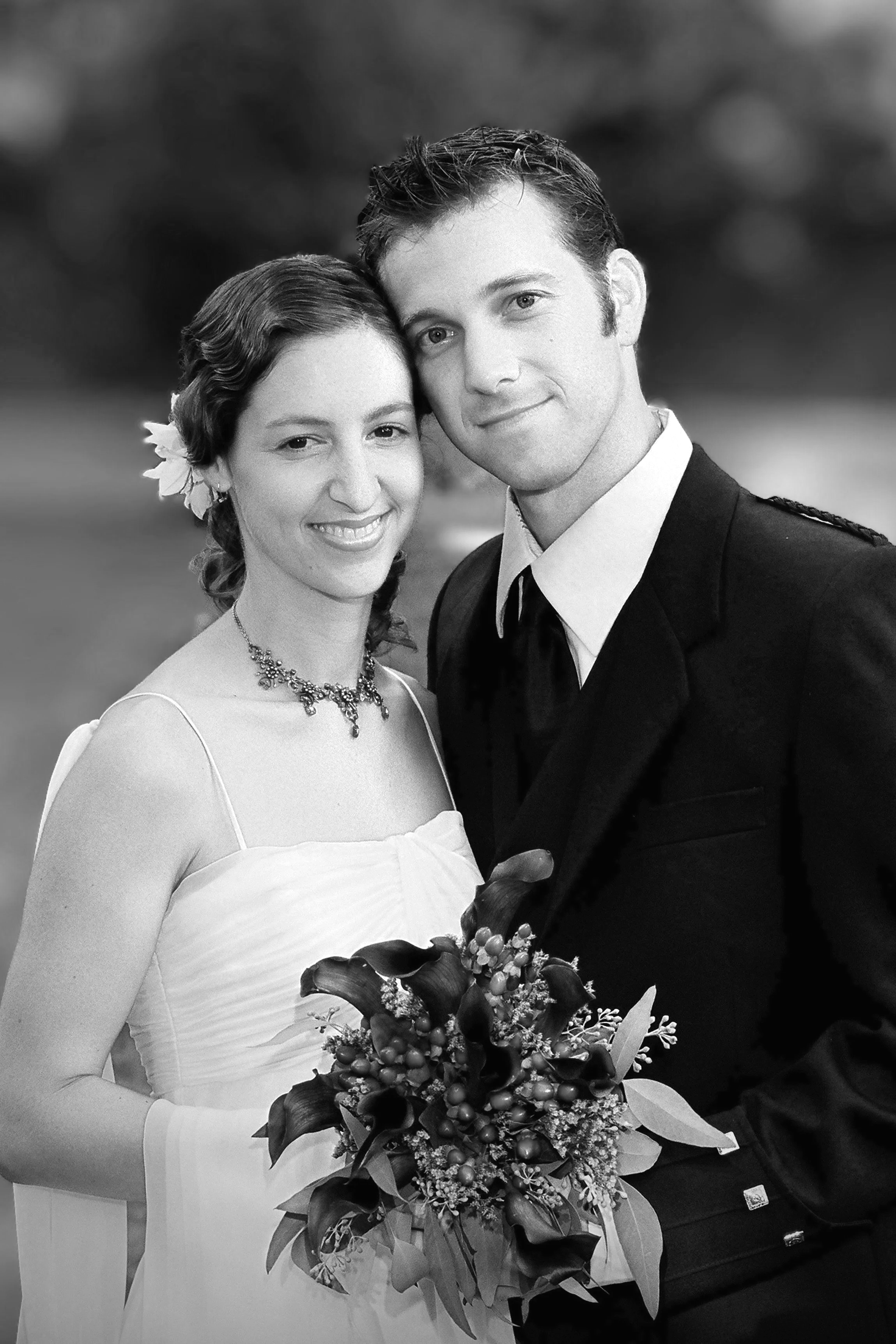 A black and white photo of a man and a woman in formal attire, with the woman holding a bouquet of flowers. They are smiling and standing close together.