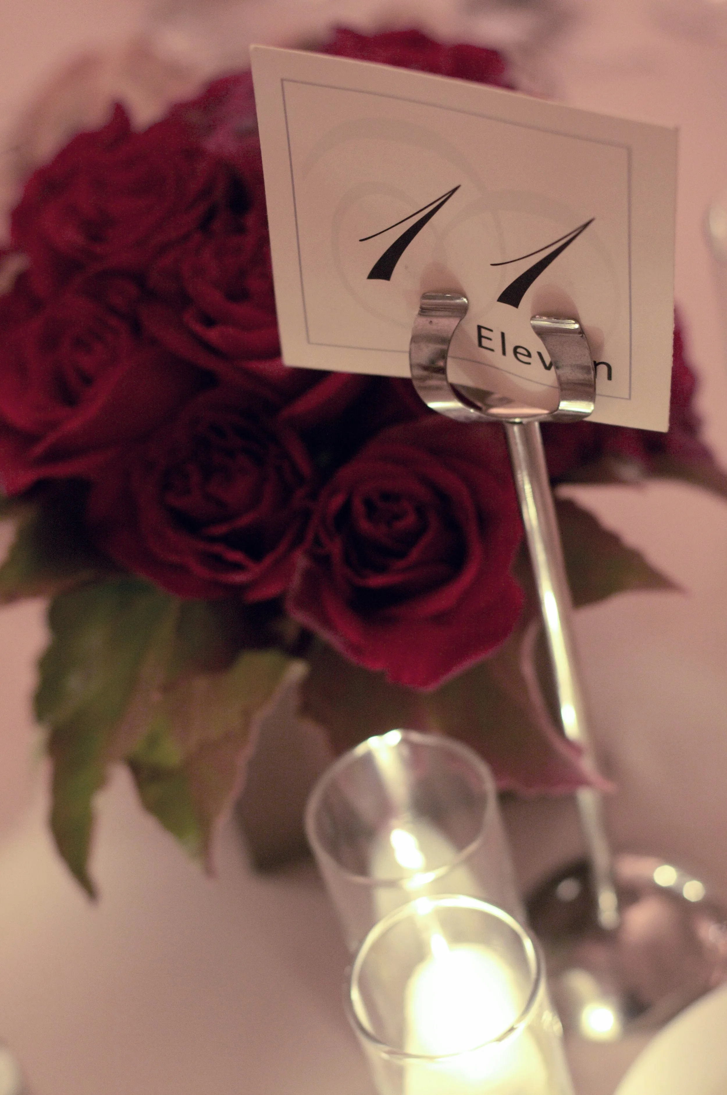 A bouquet of red roses with green leaves and a small card attached, placed near some candles that are lit, creating a warm and romantic scene.