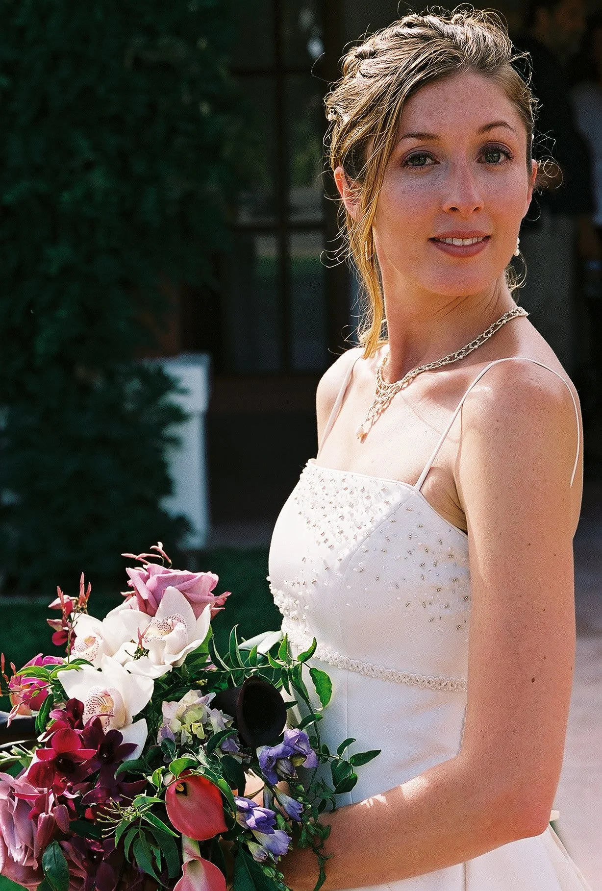 A woman in a white dress holding a bouquet of flowers, smiling outdoors.