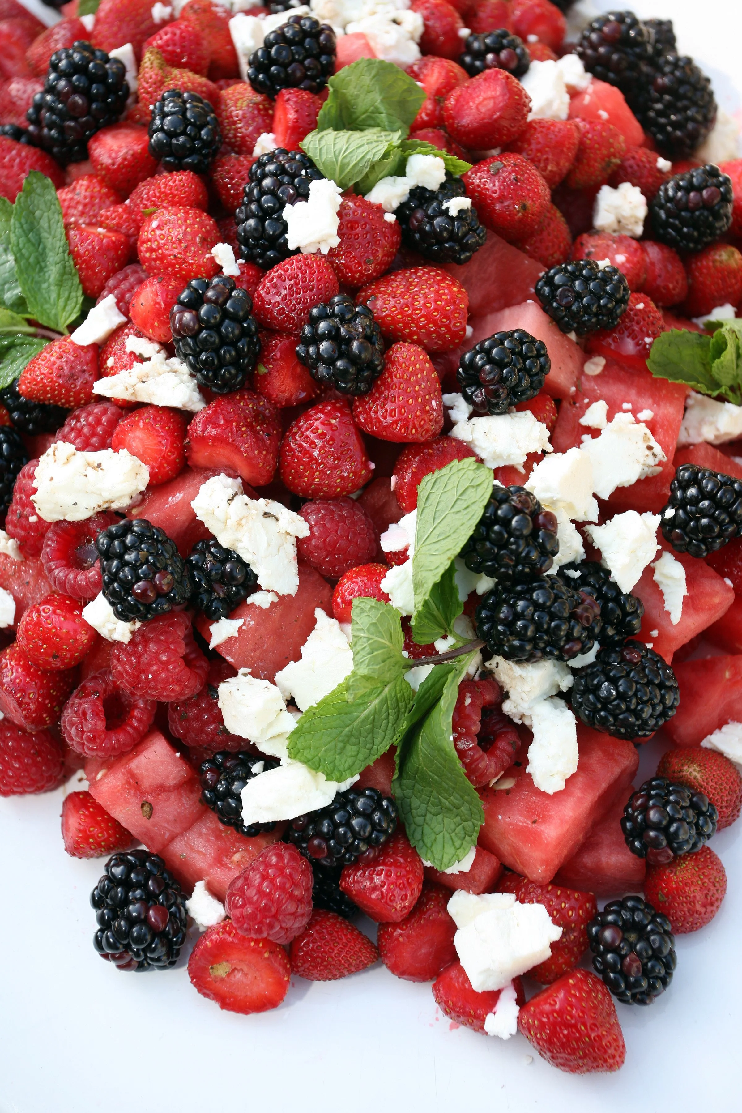 Scenery food close-up view of a fruit salad with strawberries, blackberries, and pieces of feta cheese, garnished with mint leaves.