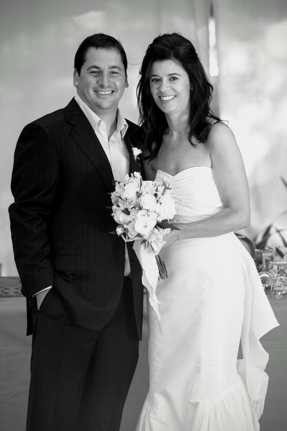 A smiling bride and groom pose together, with the bride holding a bouquet of flowers at their wedding reception.