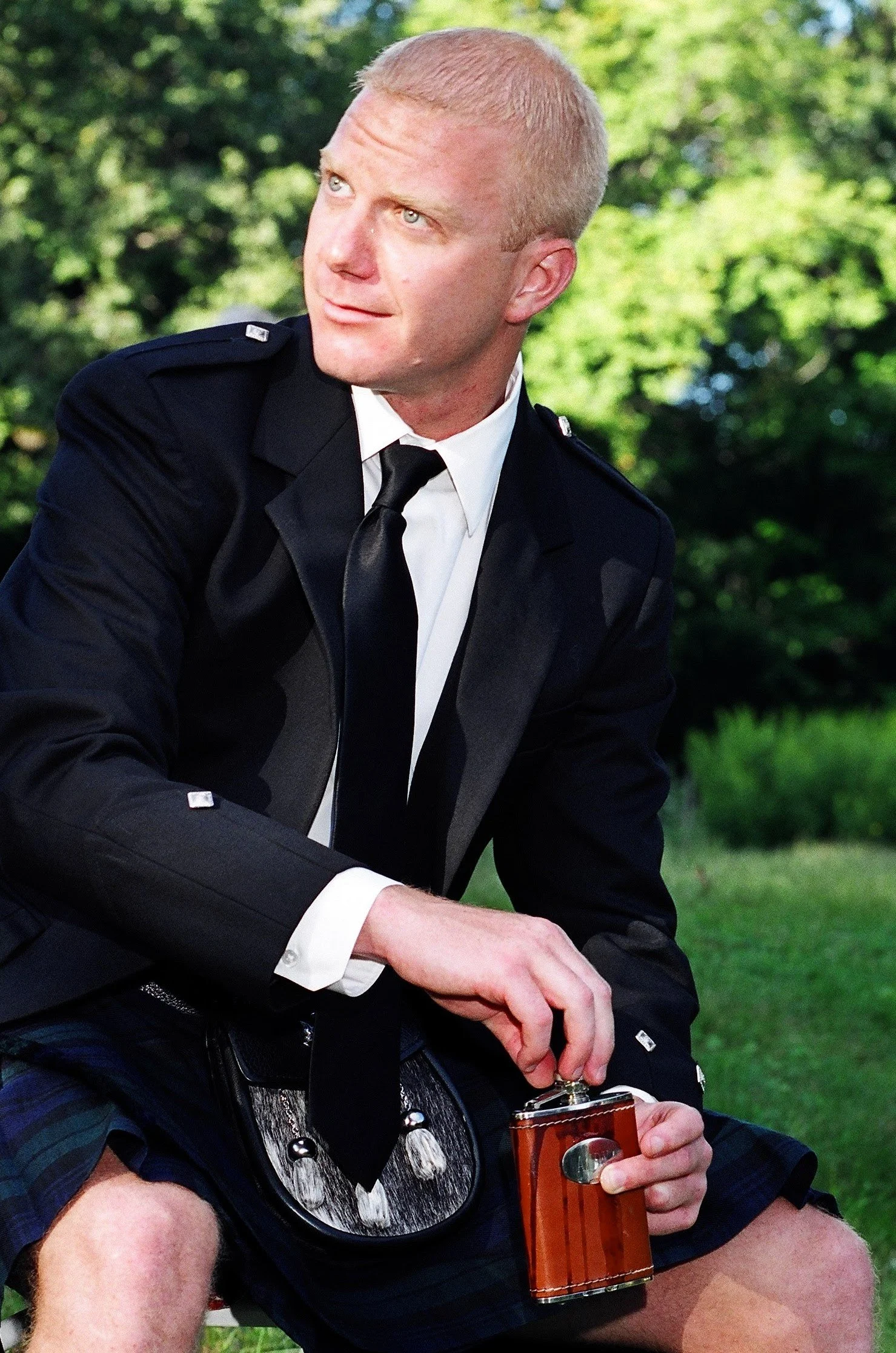 A man dressed in a police uniform sitting outdoors, holding a small brown flask.
