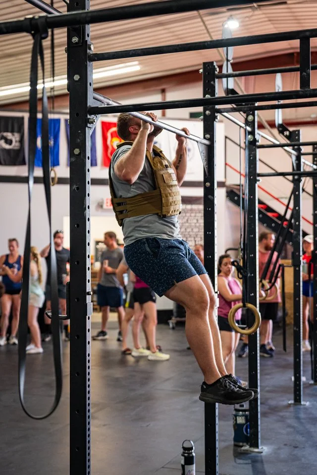 Person doing pull-up exercise on gym equipment in a busy gym setting.