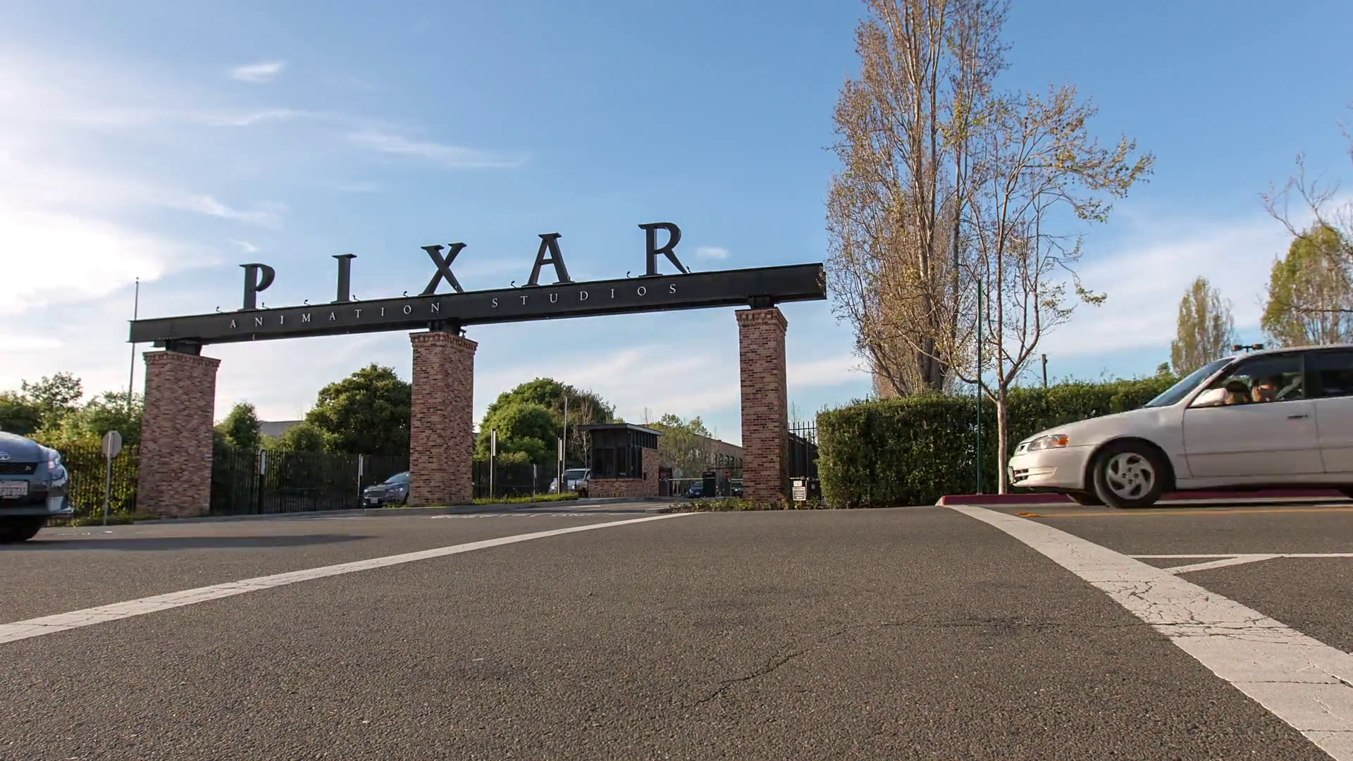 Entrance to Pixar Animation Studios with a large sign on brick pillars and cars driving on the street in front.