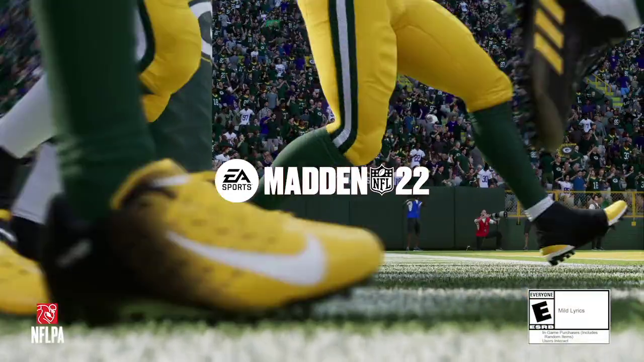 Close-up view of an aggressive green and yellow football player wearing yellow cleats, with a packed football stadium in the background during a game. The Madden NFL 22 logo is prominently displayed in the center with the EA Sports logo beside it.
