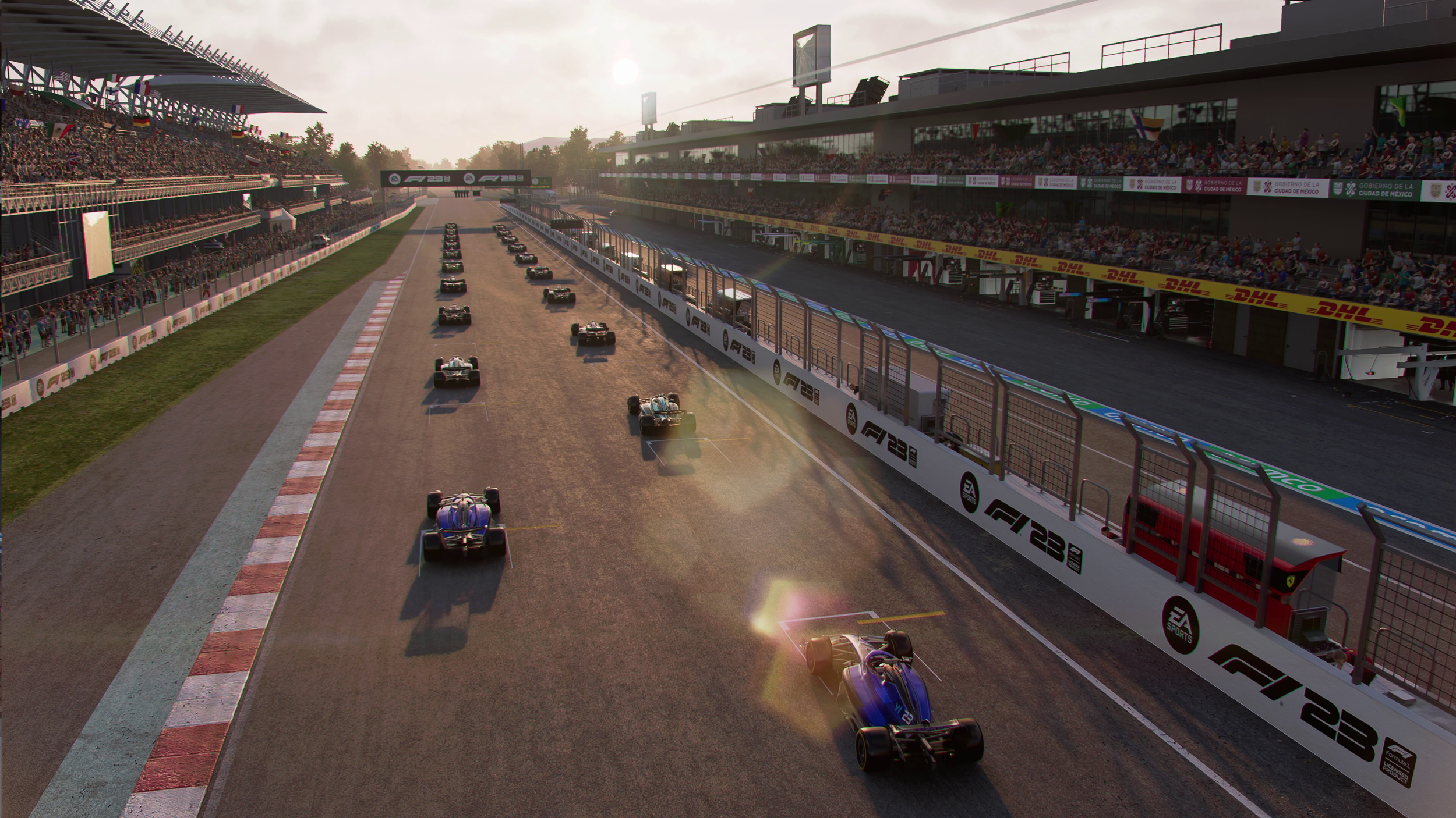 Race cars on a dirt track at a motorsport race, with spectators in stadium stands on both sides and sunlight in the background.
