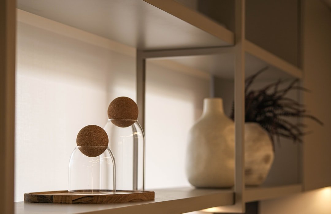 Decorative glass cloches with cork balls on a wooden tray, a large ceramic vase, and a plant on a white shelf.
