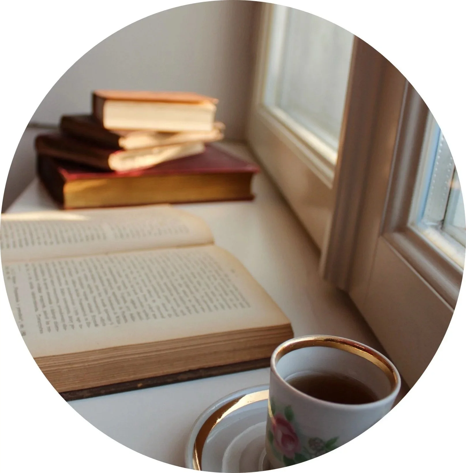 An open book with printed text, a stack of closed books, a cup of coffee with a floral pattern, and sunlight coming through a window.
