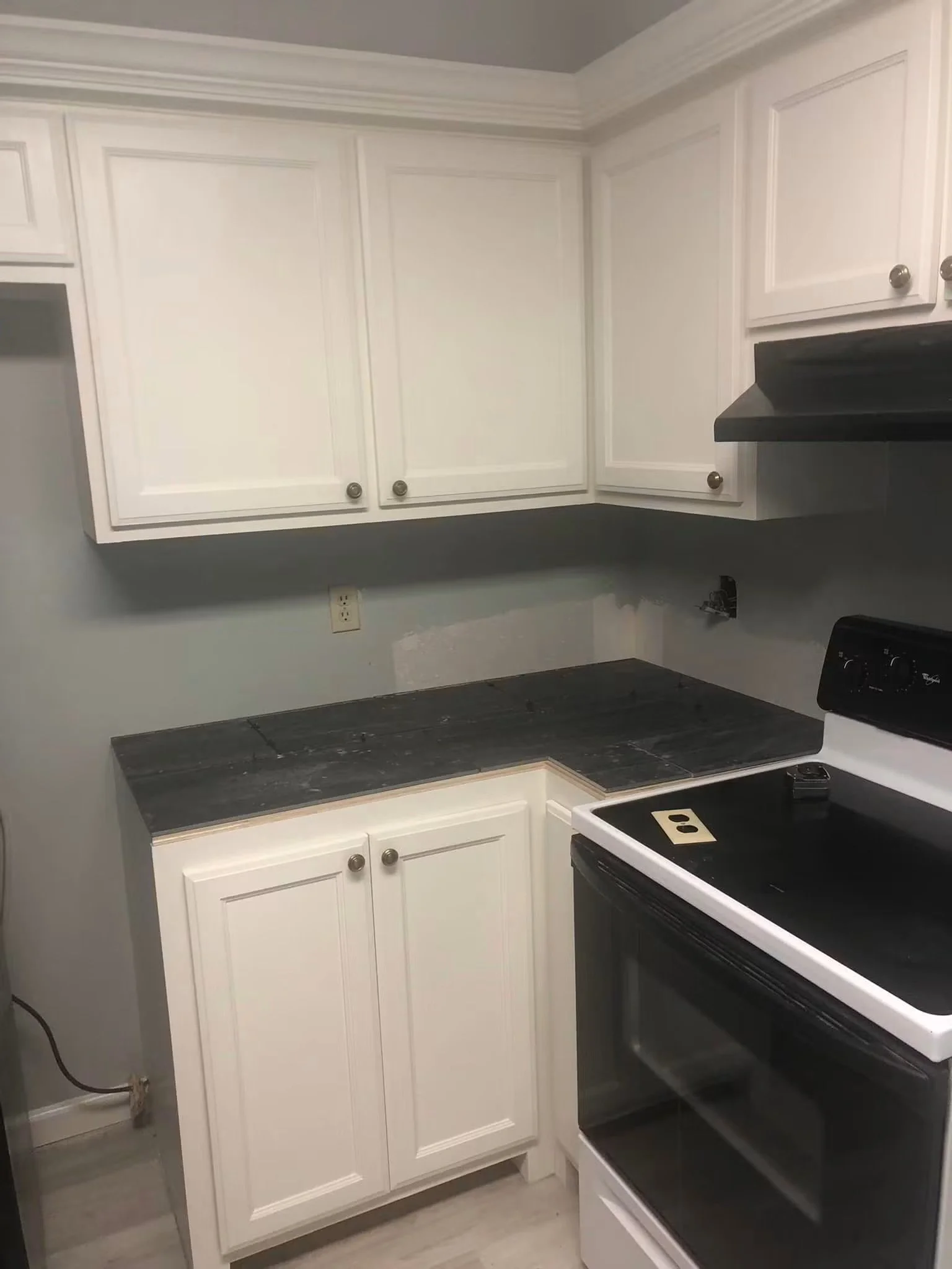 A kitchen with white cabinets above and below a dark gray countertop, a black stove, and an electrical outlet on the wall.