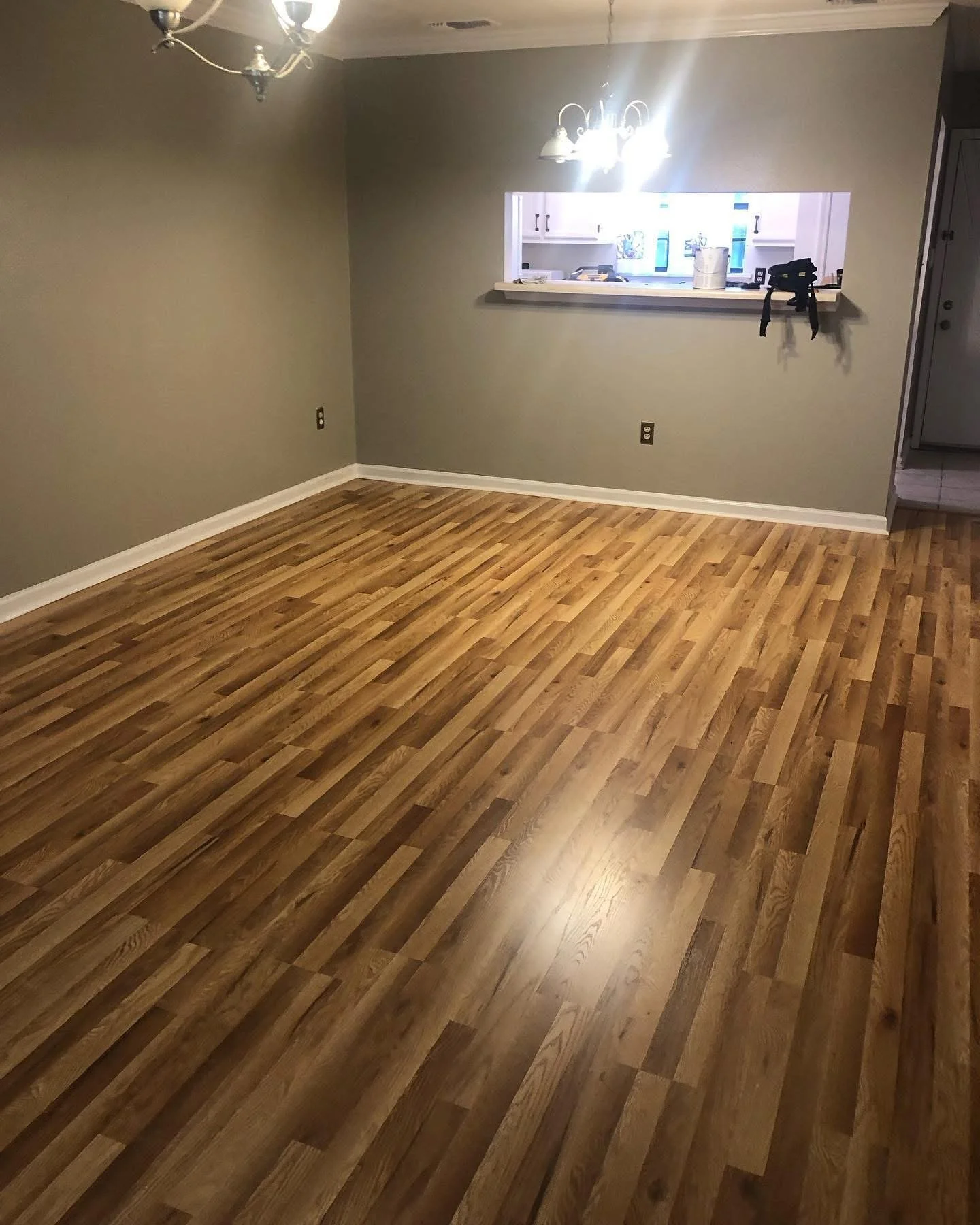 Empty living room with wood laminate flooring, beige walls, ceiling light, and kitchen opening.