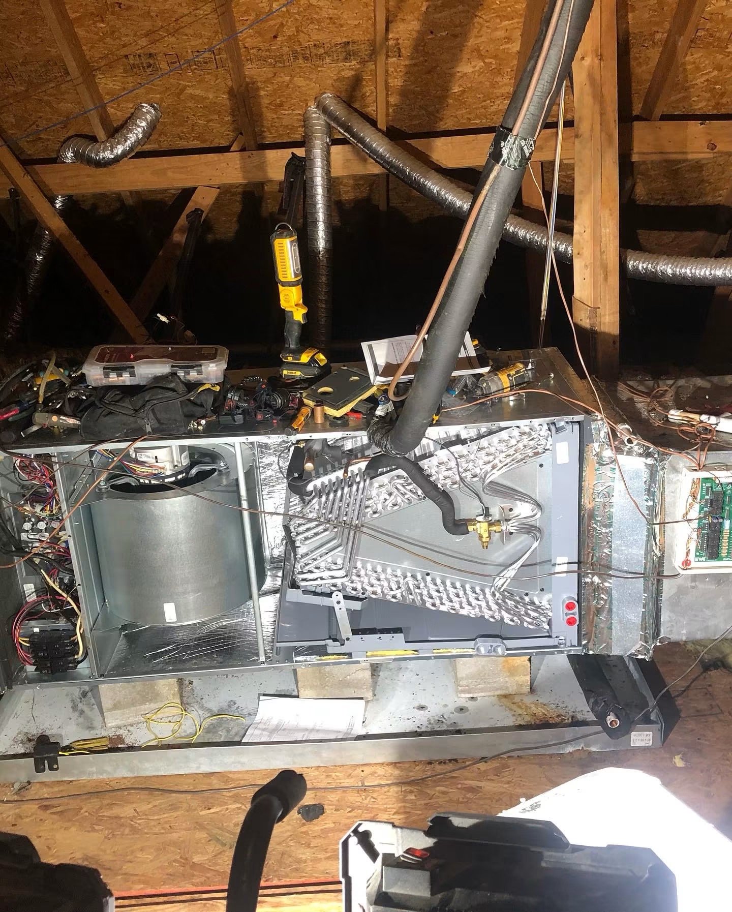 Open metal furnace or HVAC unit with internal wiring and components exposed, situated in an attic or unfinished space with wooden beams and insulation.