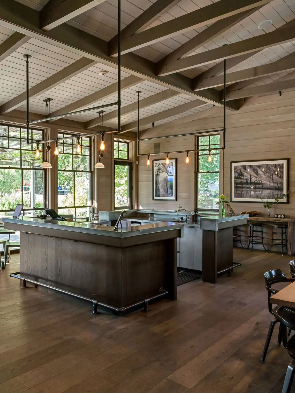 Modern rustic bakery with wood-paneled walls, large windows, pendant lights, and a stainless steel counter.