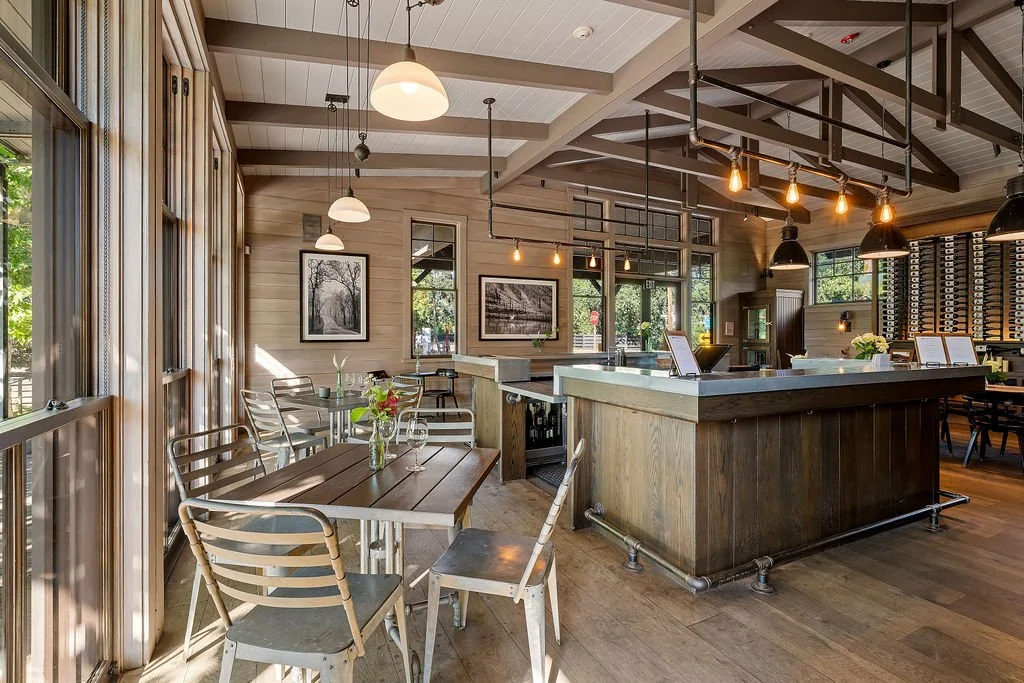 Interior of a cozy restaurant with wooden paneling, large windows, industrial lighting, and a central bar.