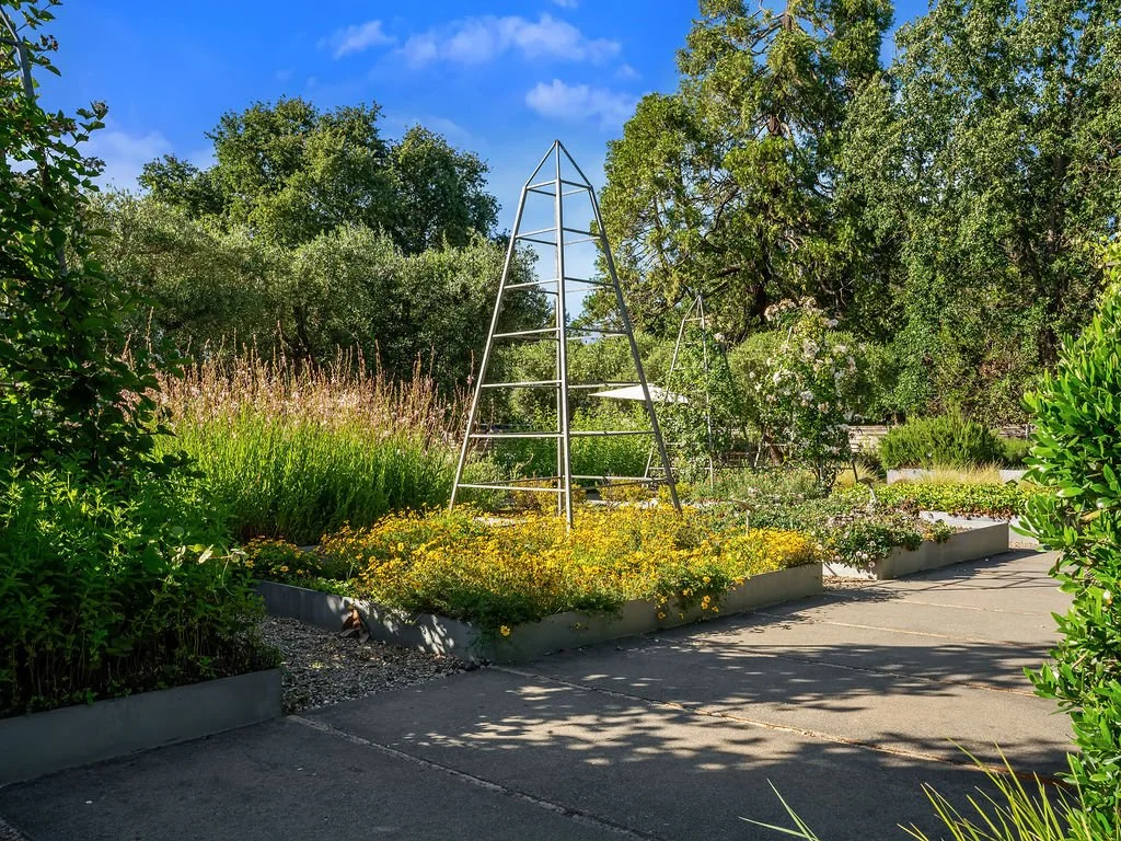 A garden with lush green trees and various flowering plants, including flowering bushes and flower beds, with a clear blue sky overhead.