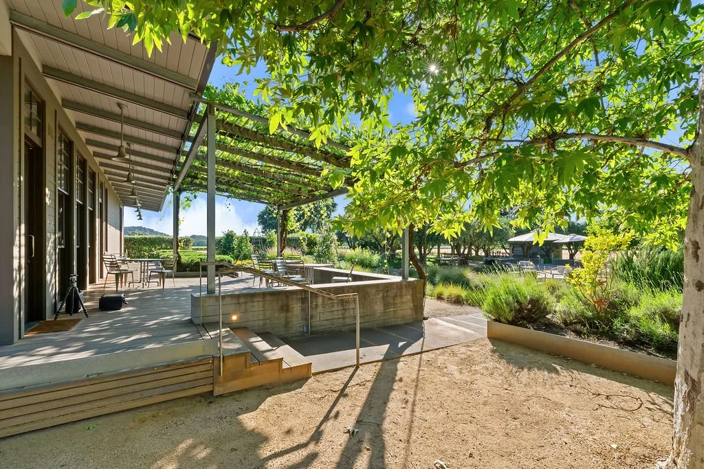Outdoor patio with seating area, green trees, and lush landscaping on sunny day.