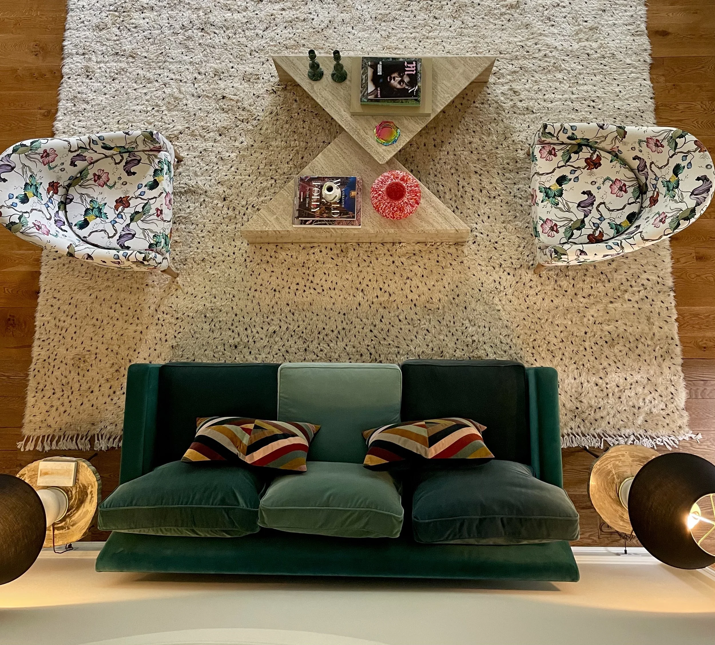 Overhead view of a seating group with a dark green velvet sofa, two floral armchairs and travertine triangular tables on a shaggy rug