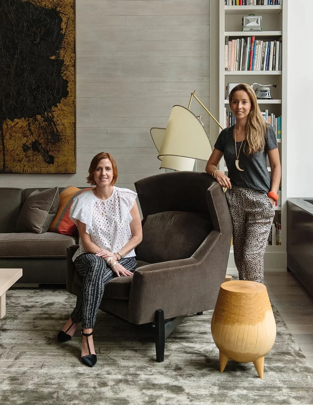 Two women in the Bond St living room beside an abstract painting and a sculptural lamp