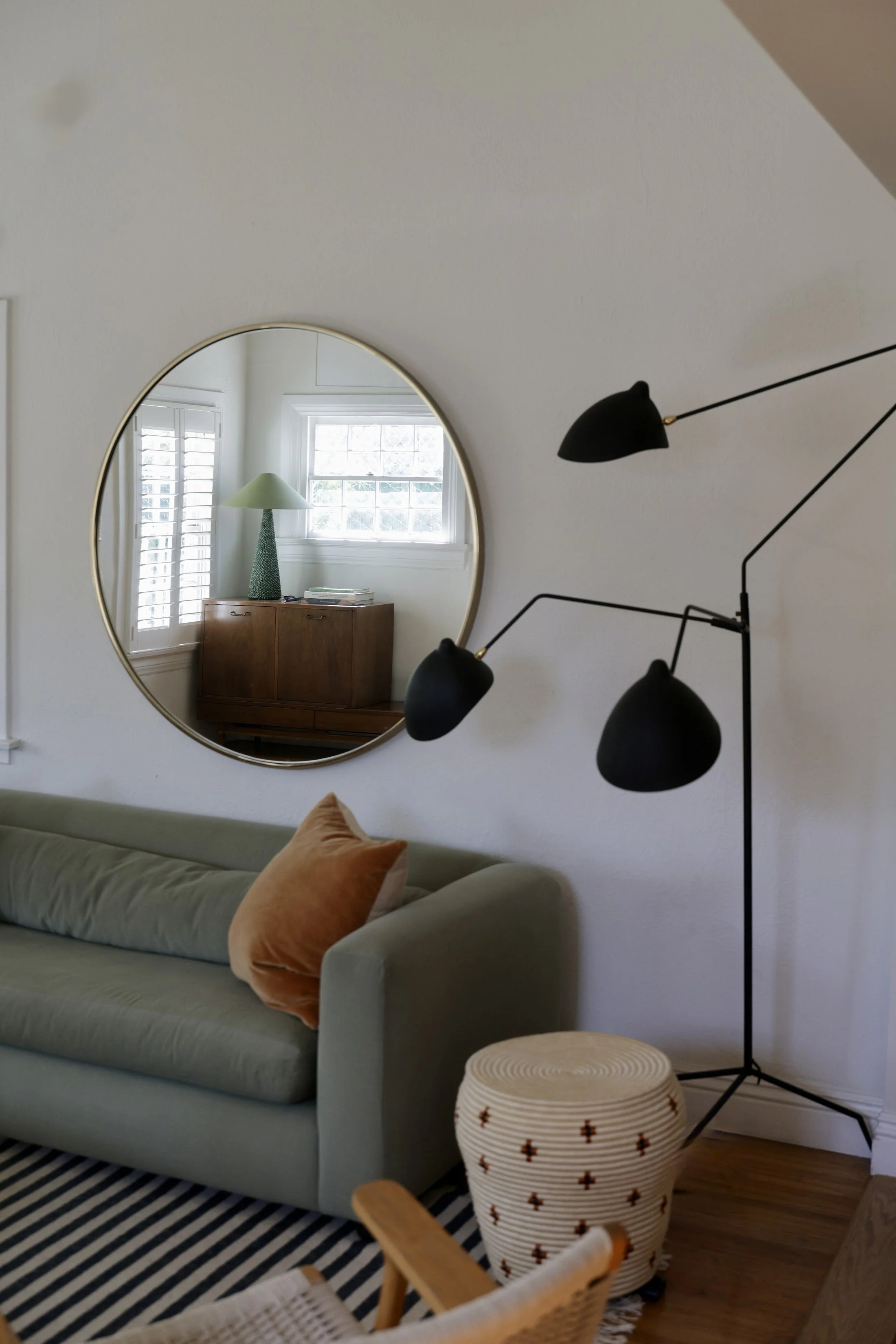 Modern living room with a round mirror, sage sofa and black articulated floor lamp