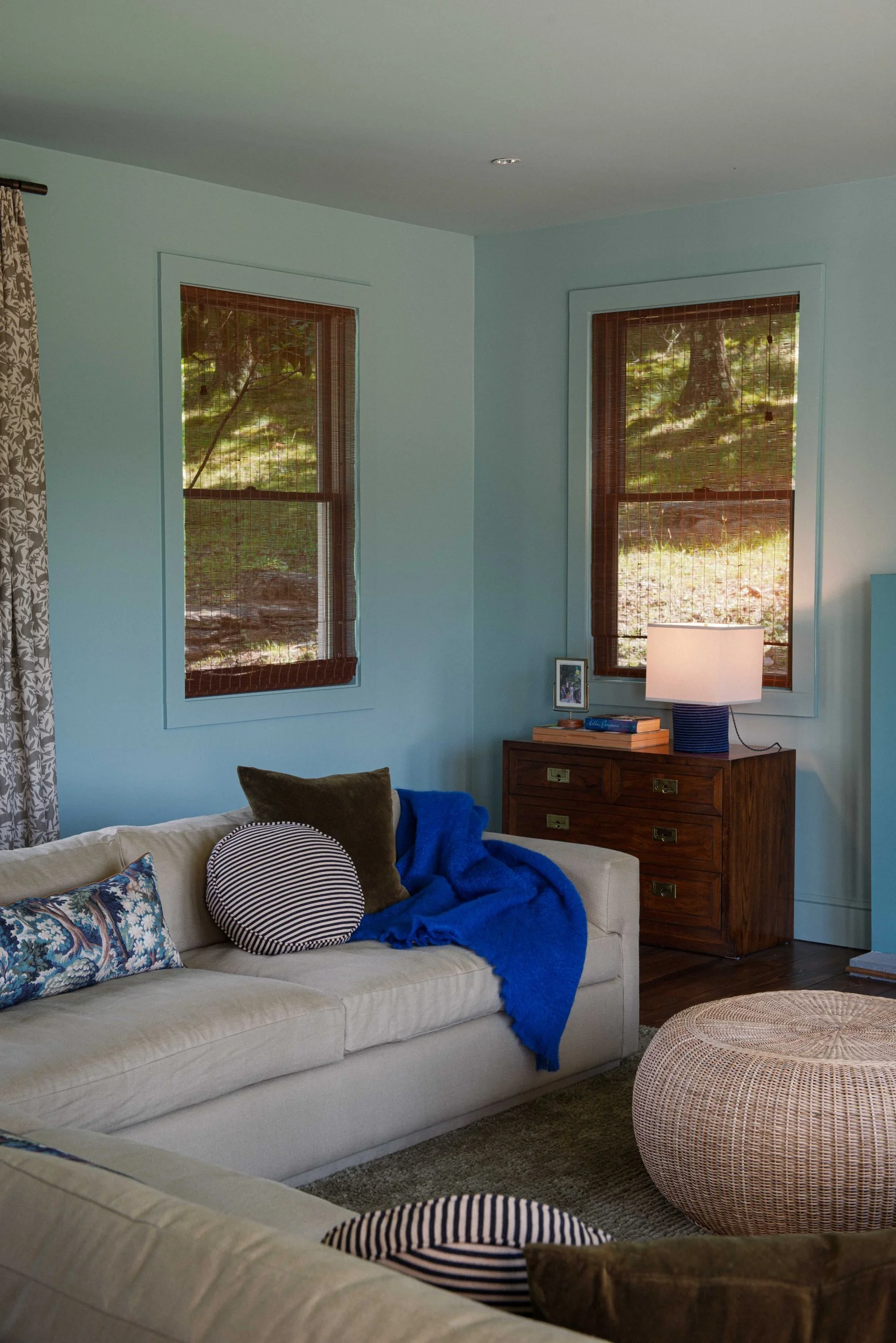 Silvernails sitting room with pale blue walls, a white sofa, woven pouf and cobalt throw