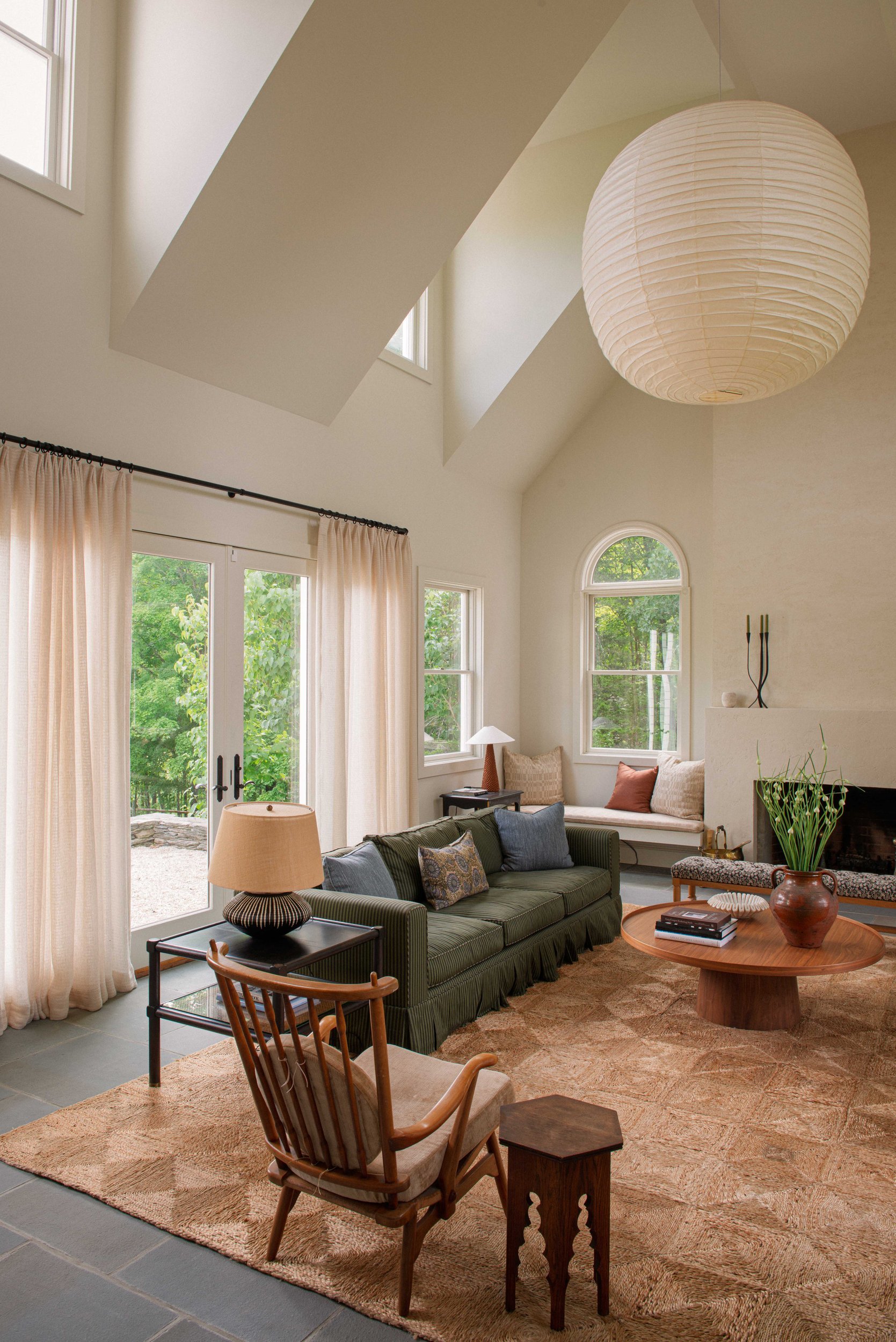 Great room with a paper globe pendant, a green striped sofa, sheer linen curtains and a jute rug over a bluestone floor