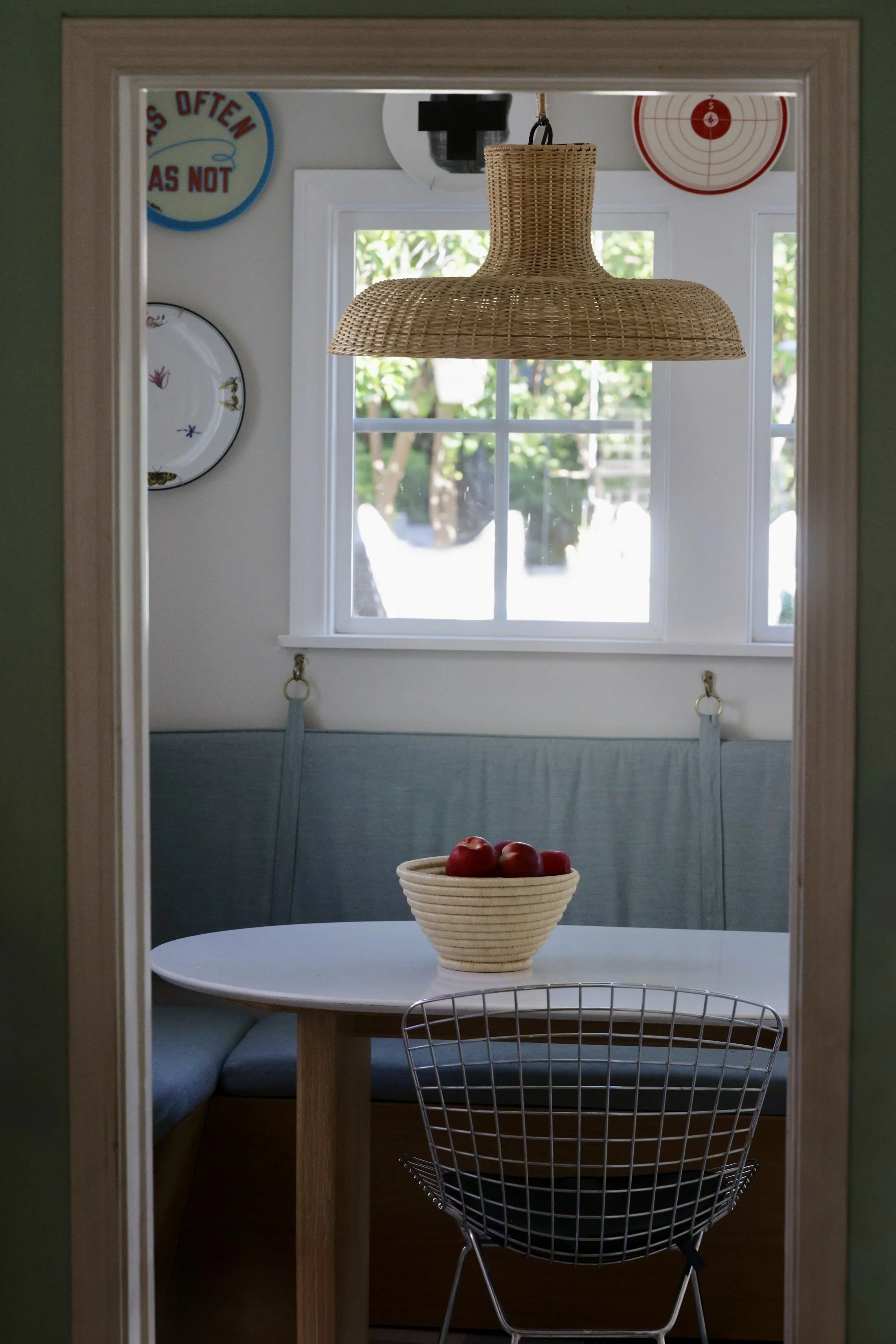 Breakfast nook with a round table, wire chair, woven pendant light and pale blue banquette