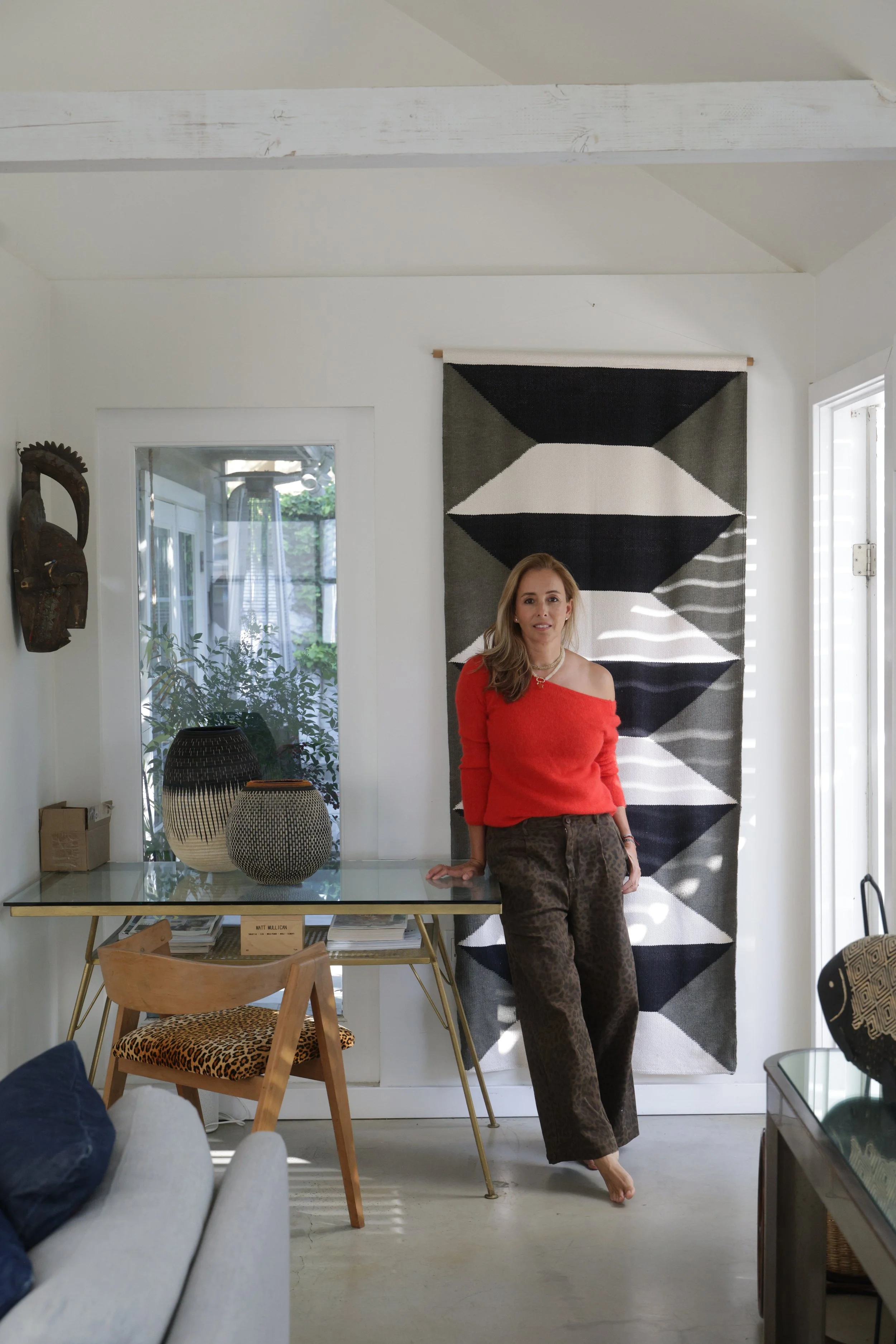 Melissa Pinto in her studio, beside a glass-topped desk and a woven black and white wall hanging