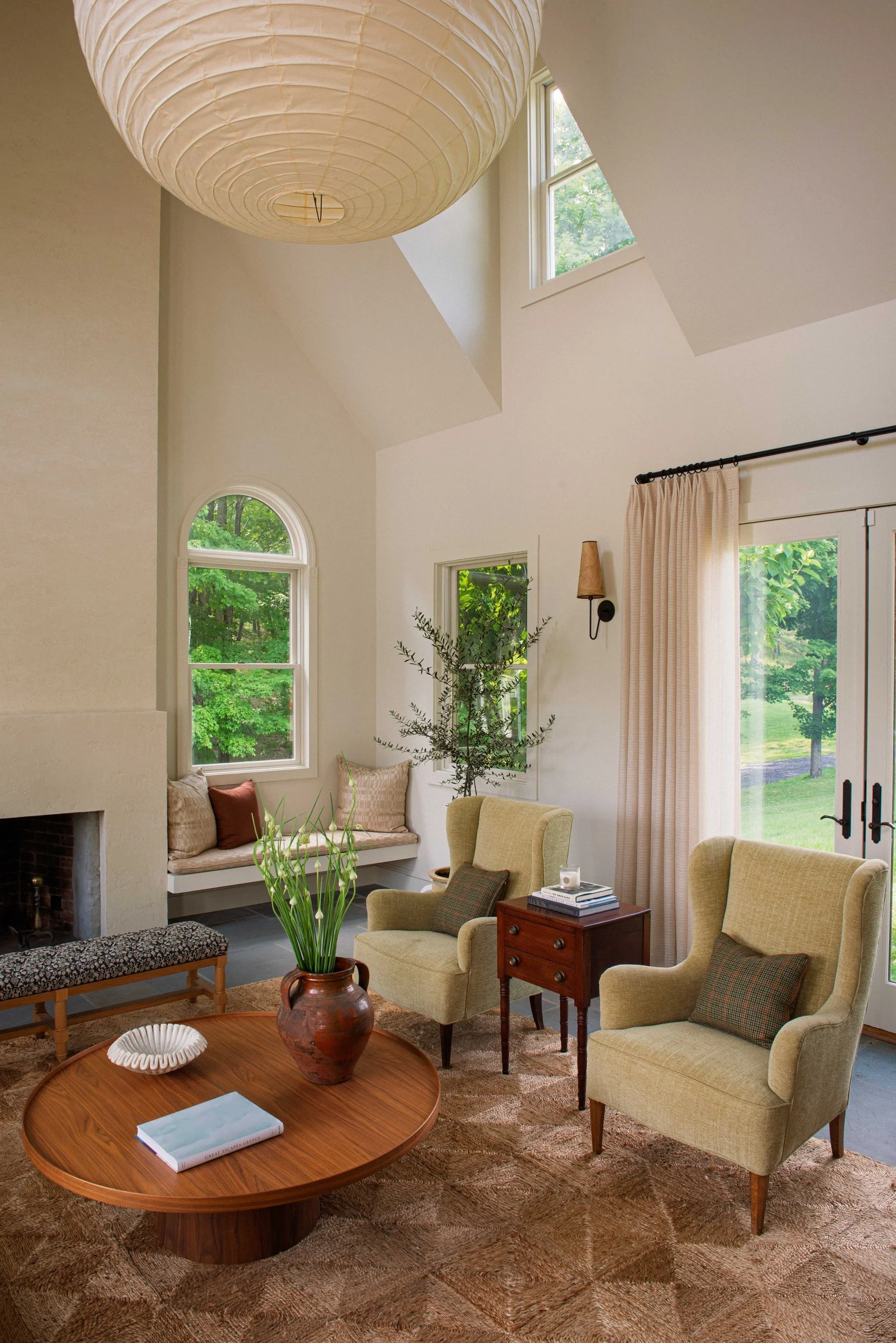 Great room with a vaulted ceiling, a plaster fireplace, built-in window seats and olive wingback chairs