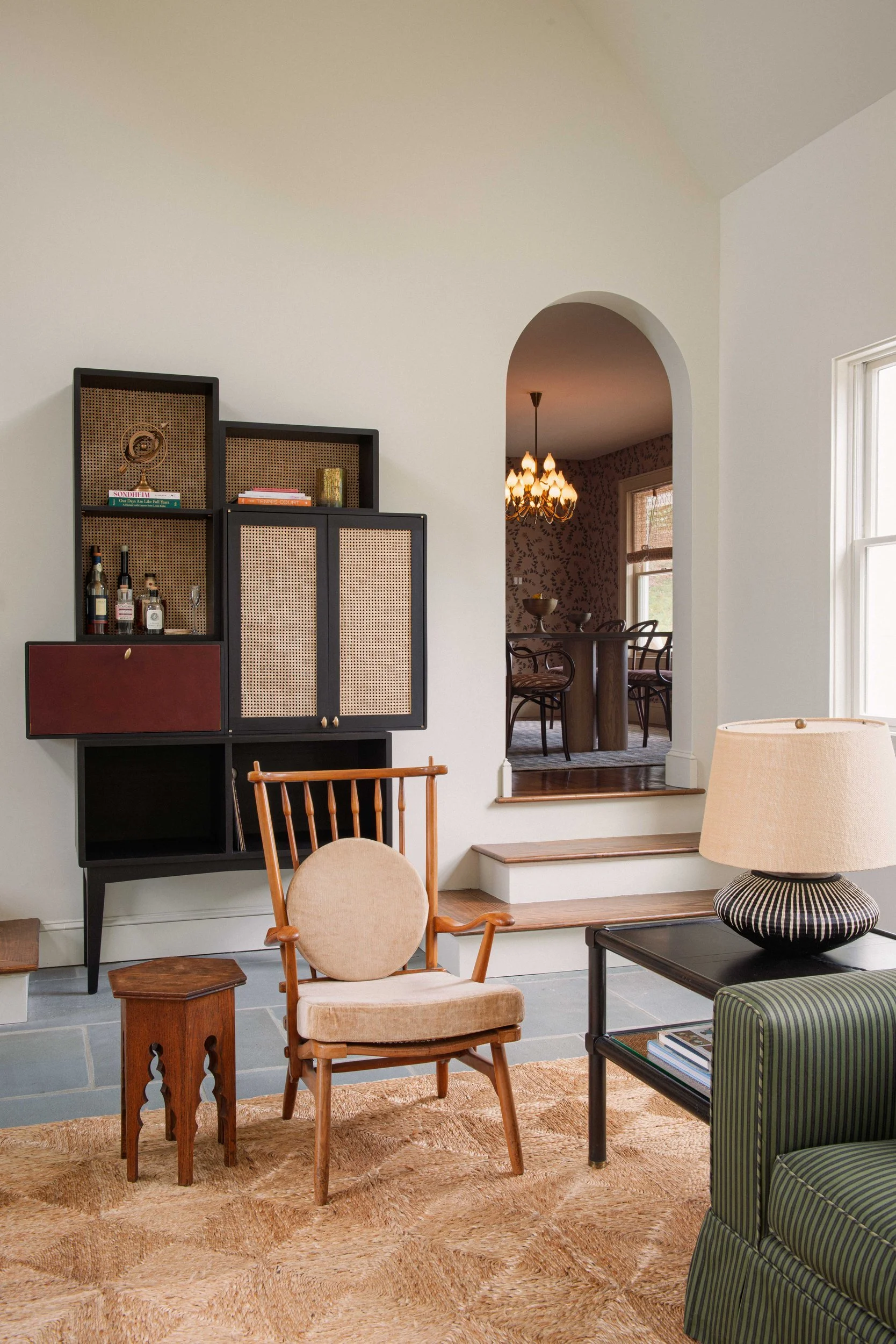Great room corner with a black caned bar cabinet, a spindle-back armchair and an arched opening onto the wallpapered dining room