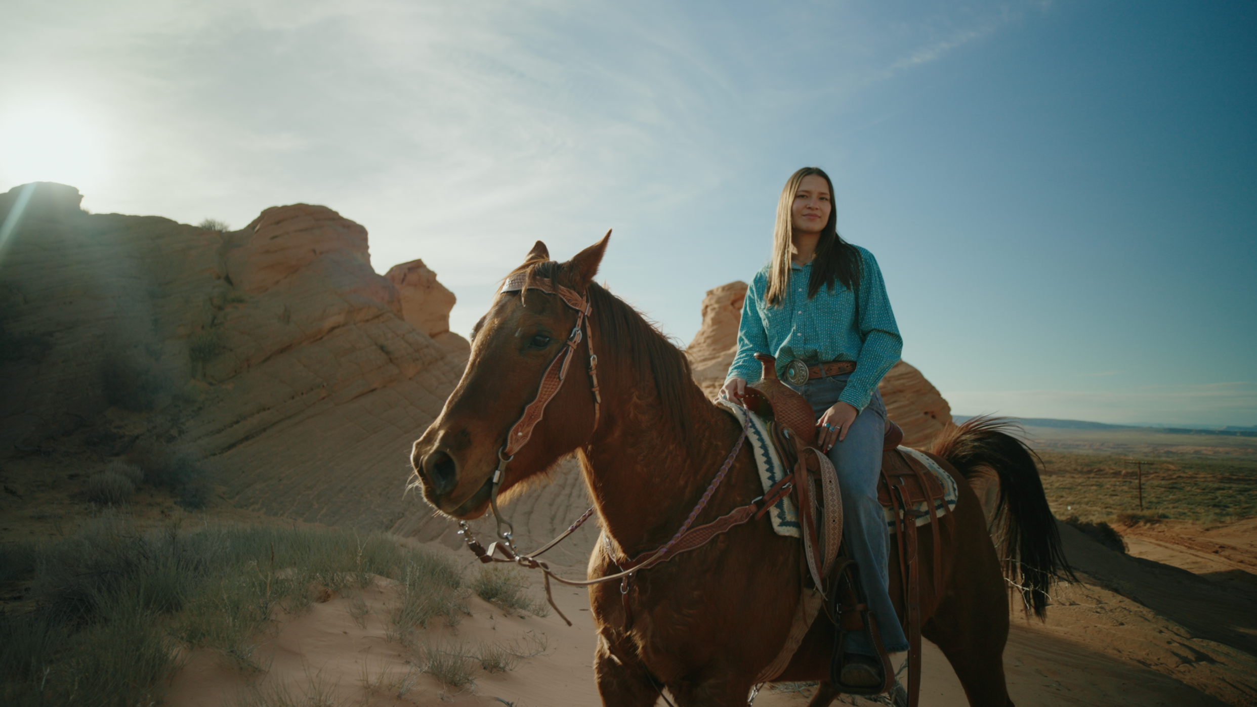 A woman riding a horse in a desert landscape with rocky formations and a clear blue sky.