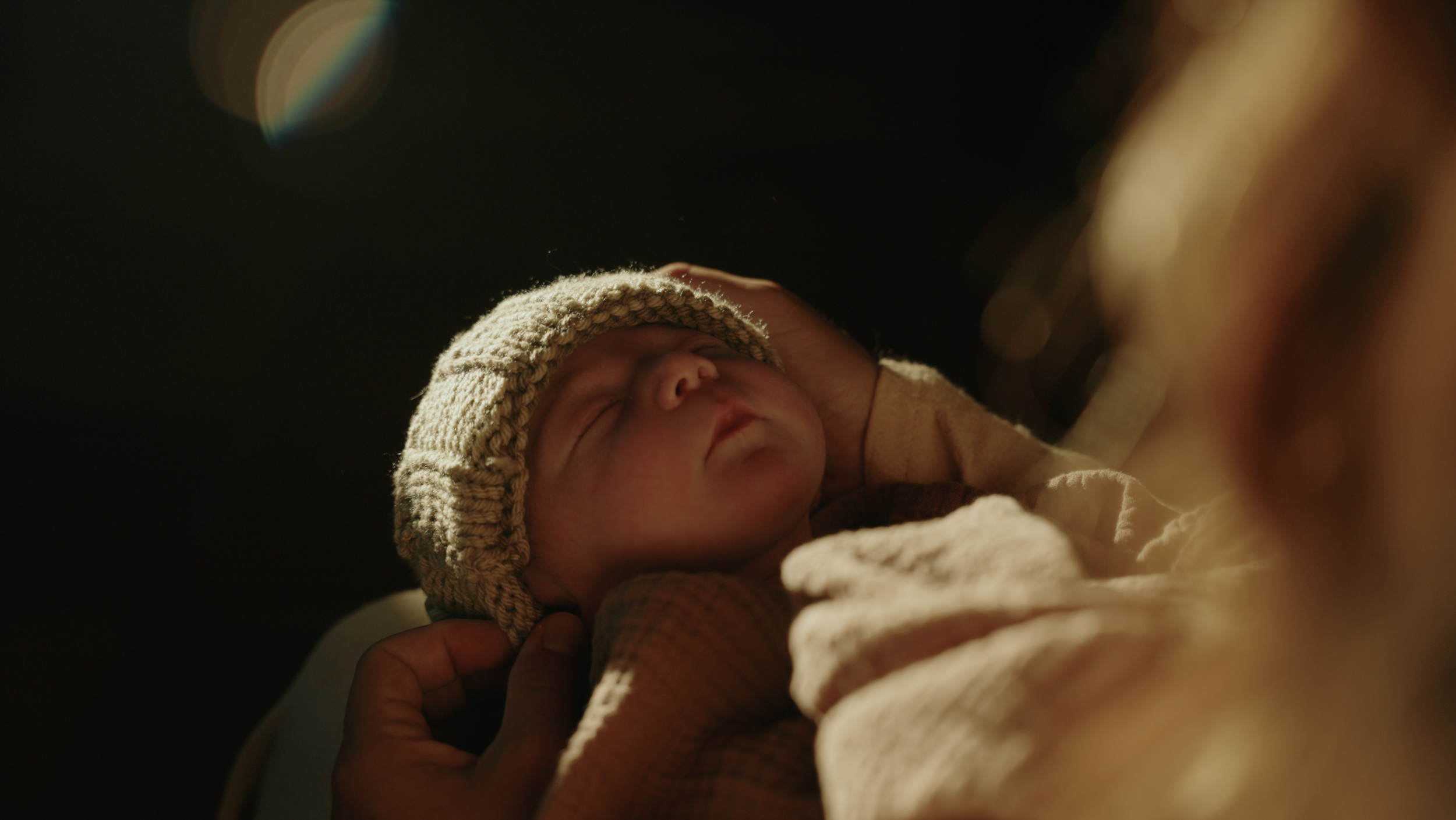 A sleeping newborn baby wearing a knitted hat and wrapped in a blanket.