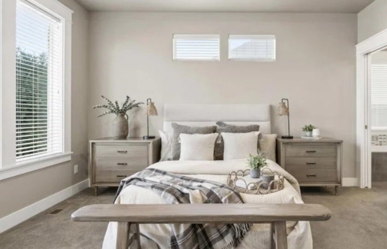 A bedroom with a bed, two nightstands, and decorative pillows, in a neutral color palette.