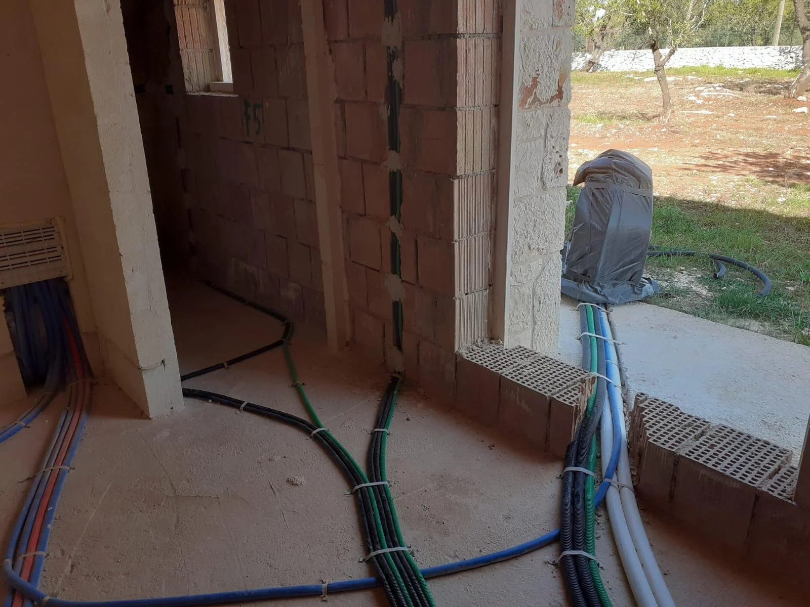 Construction site showing interior and exterior walls with exposed brick and wires on the floor, with some pipes going outside.
