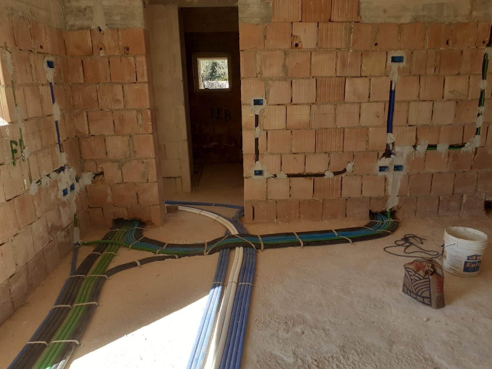 Interior of a building under construction with exposed brick walls and electrical wiring running along the floor, some with plastic conduit and junction boxes.
