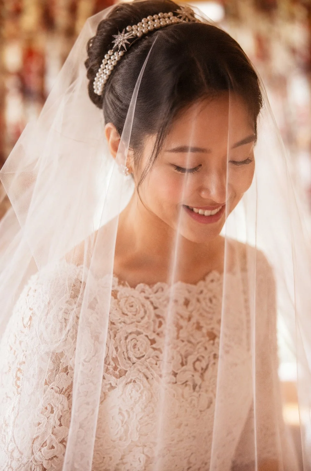 Close-up of a bride with her eyes closed, smiling gently, wearing a lace wedding dress, a pearl headpiece, and a veil.