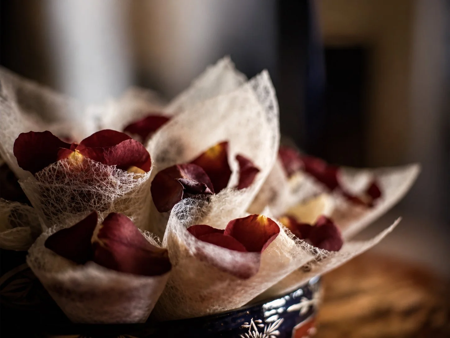 Close-up of dried rose petals on white lace fabric with a dark background.